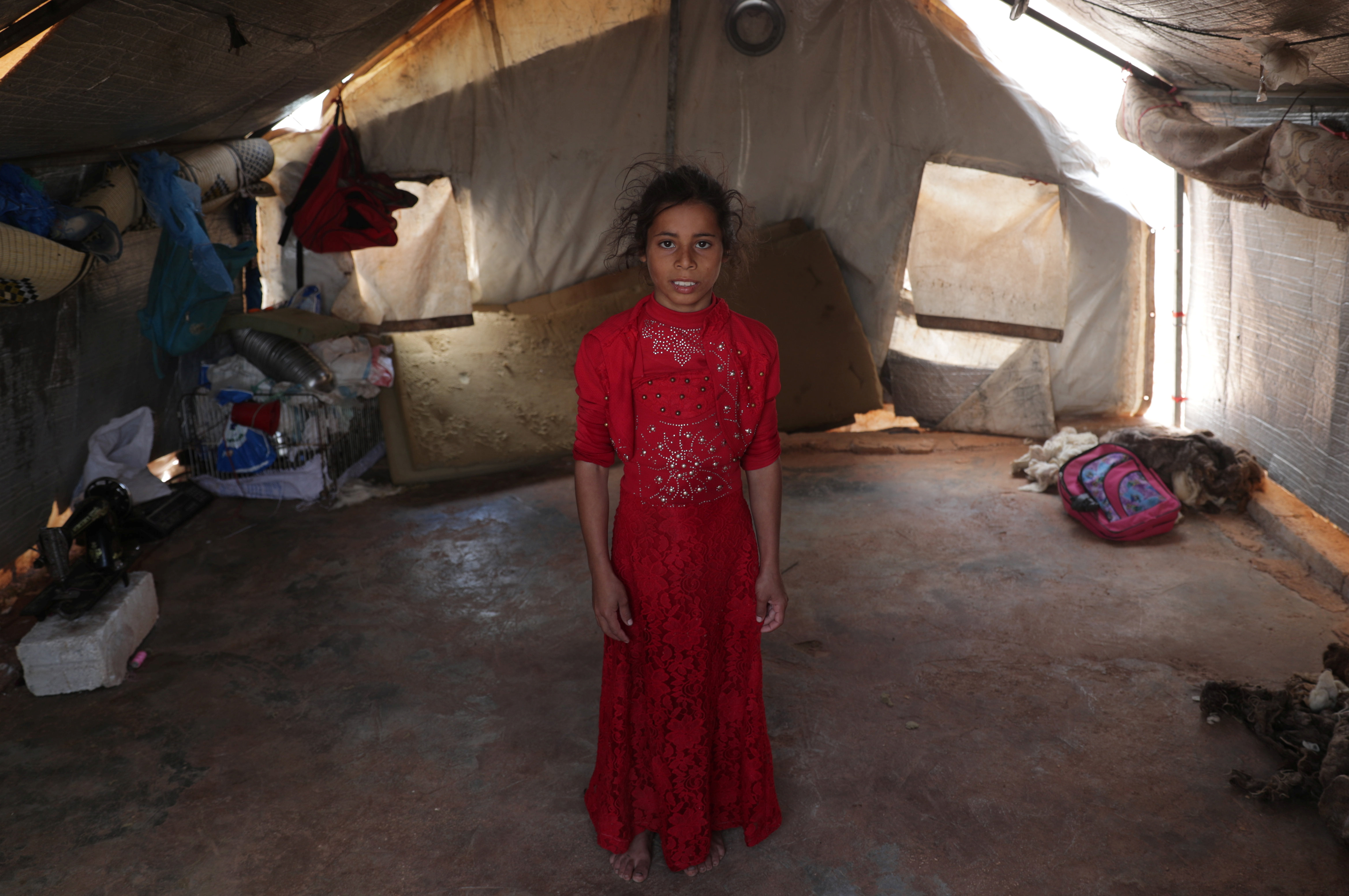 Ranim Barakat, una niña siria desplazada de nueve años del campo de Hama que nunca ha conocido la paz, sus pies descalzos asomando por debajo de un vestido rojo bordado. (REUTERS / Khalil Ashawi)