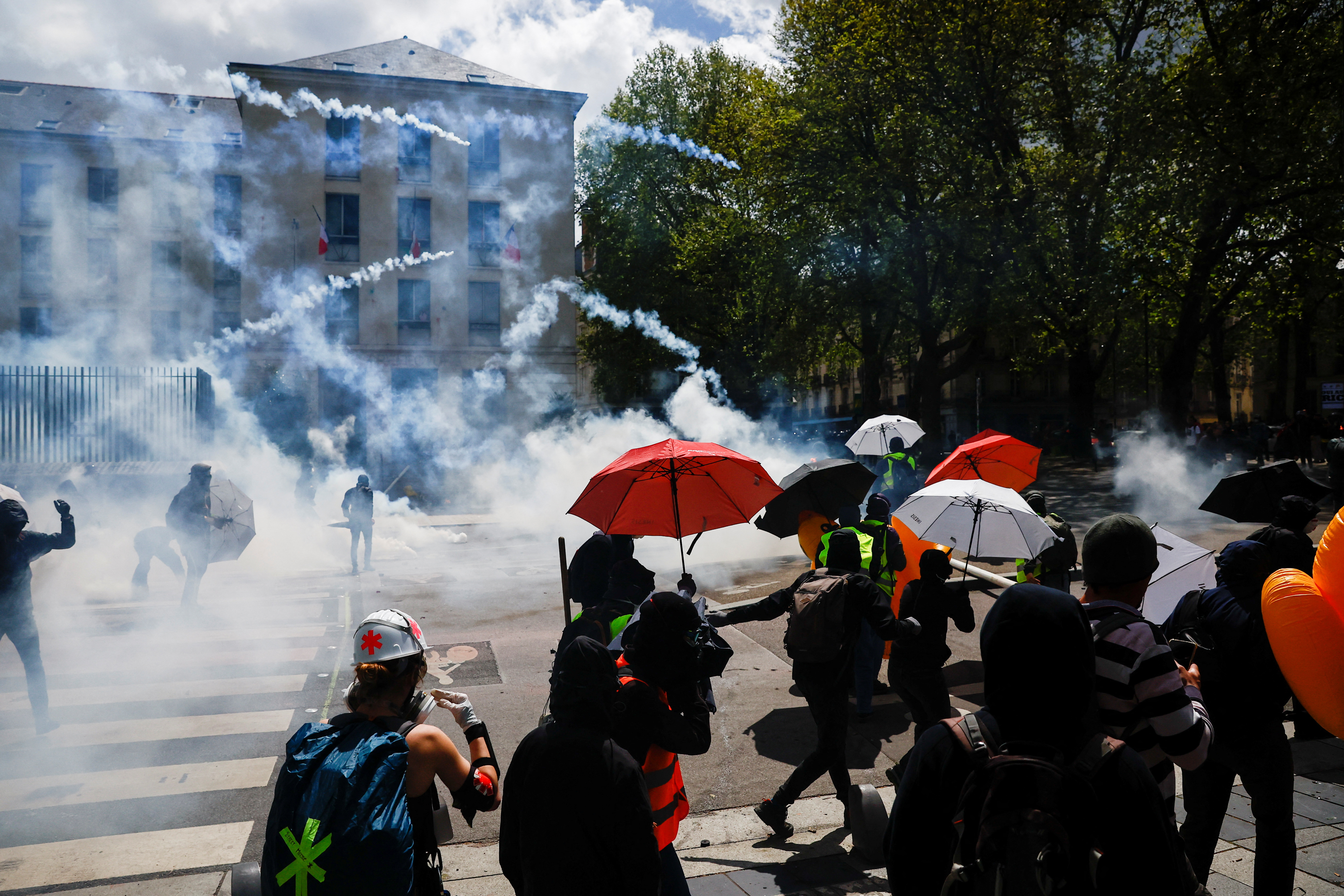 Demonstrators protect themselves with umbrellas amid tear gas during the traditional May Day labour march, a day of mobilisation against the French pension reform law and for social justice, in Nantes, France May 1, 2023. REUTERS/Stephane Mahe