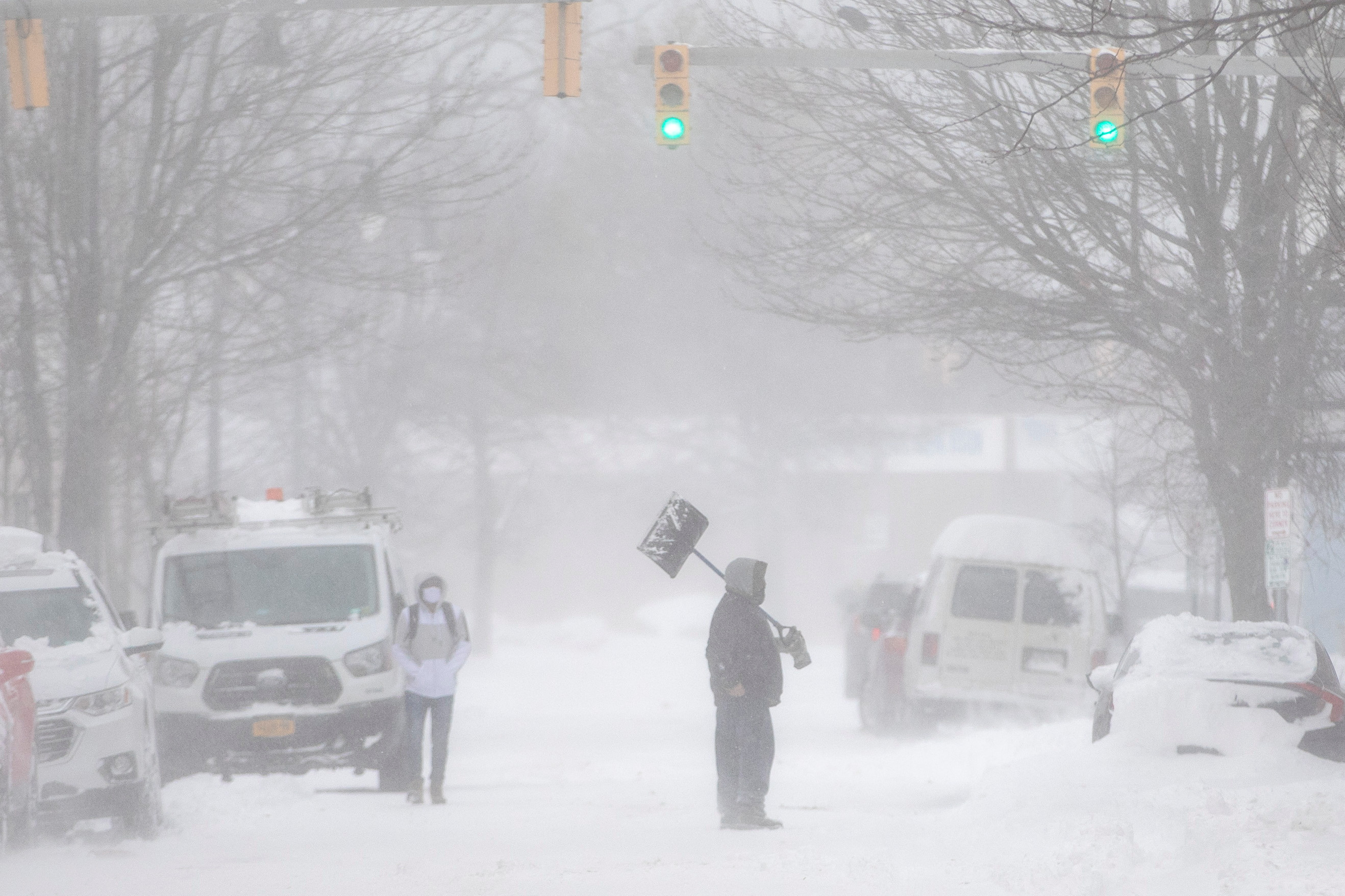 Una persona che trasporta una pala cammina in mezzo a una strada durante una tempesta di neve a Buffalo il 19 novembre 2022.