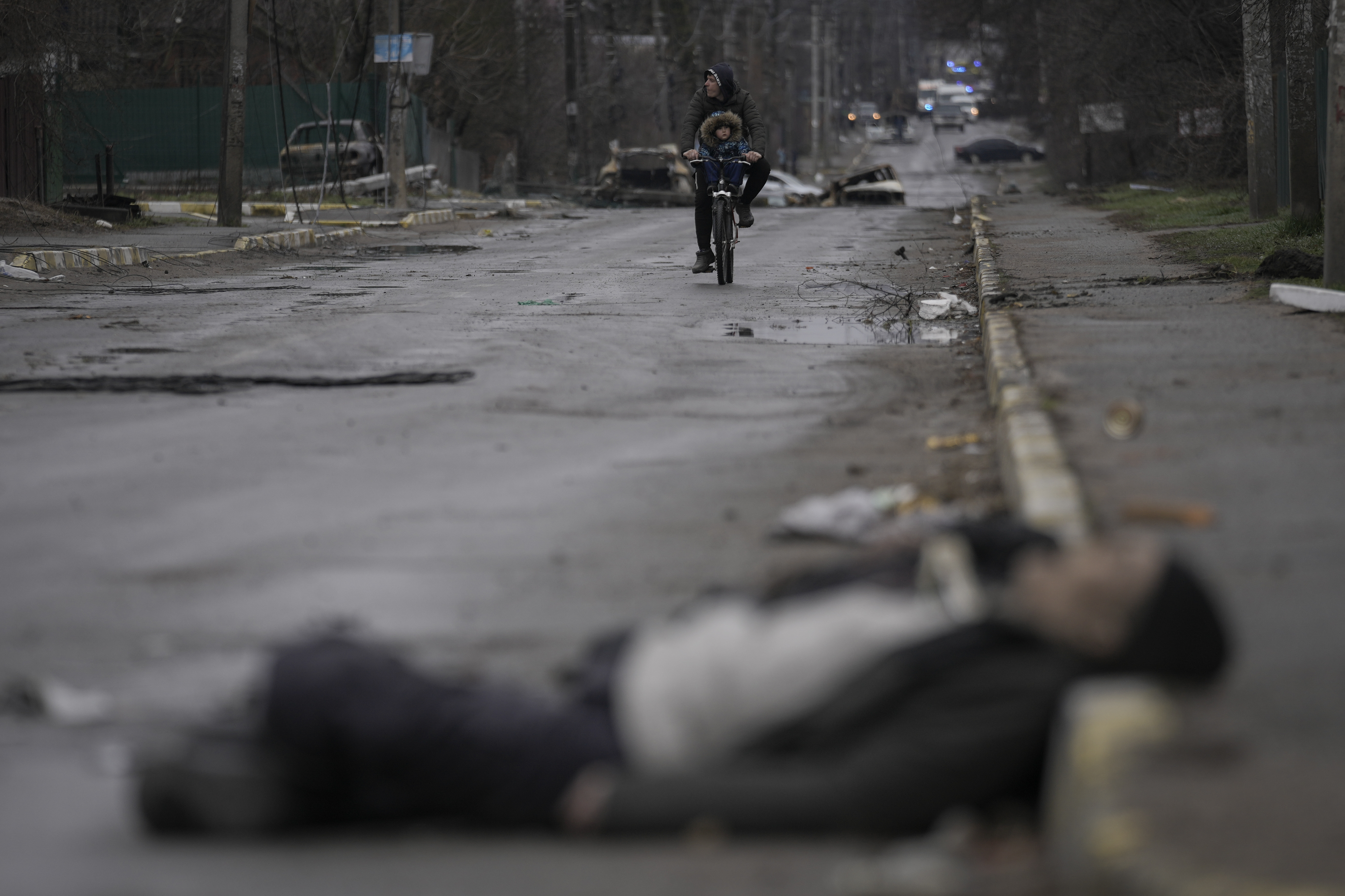 Un hombre y un niño andan en bicicleta mientras cuerpos de civiles yacen en una calle de Bucha, en las afueras de Kiev, Ucrania, el 2 de abril de 2022. Bucha, en la periferia noroccidental de la capital ucraniana, había estado ocupada por las fuerzas rusas durante aproximadamente un mes. Fue tomada mientras éstas avanzaban hacia Kiev al inicio de la invasión de Ucrania que comenzó a finales de febrero de 2022. Cuando se retiraron, dejaron a su paso escenas de horror. (AP Foto/Vadim Ghirda, Archivo)