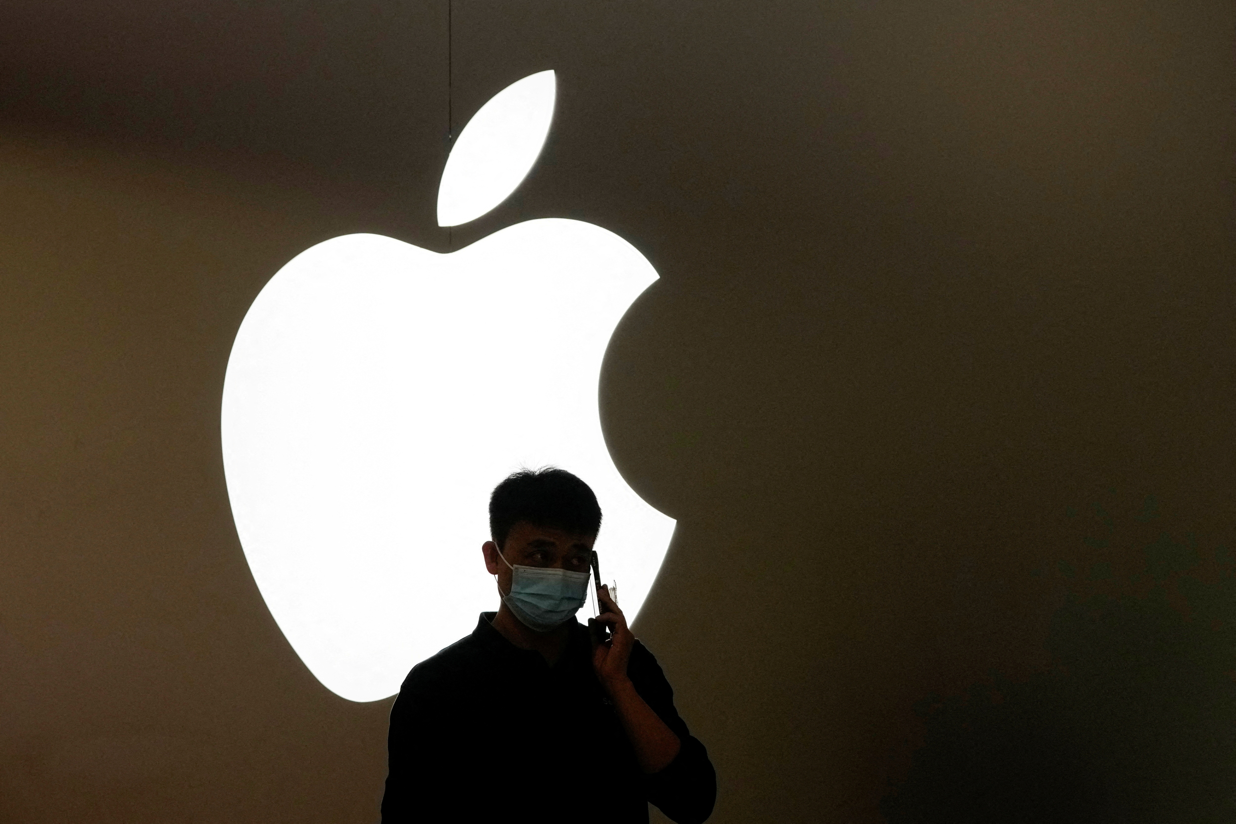 FILE PHOTO: A man talks on a phone in front of an Apple logo outside its store in Shanghai