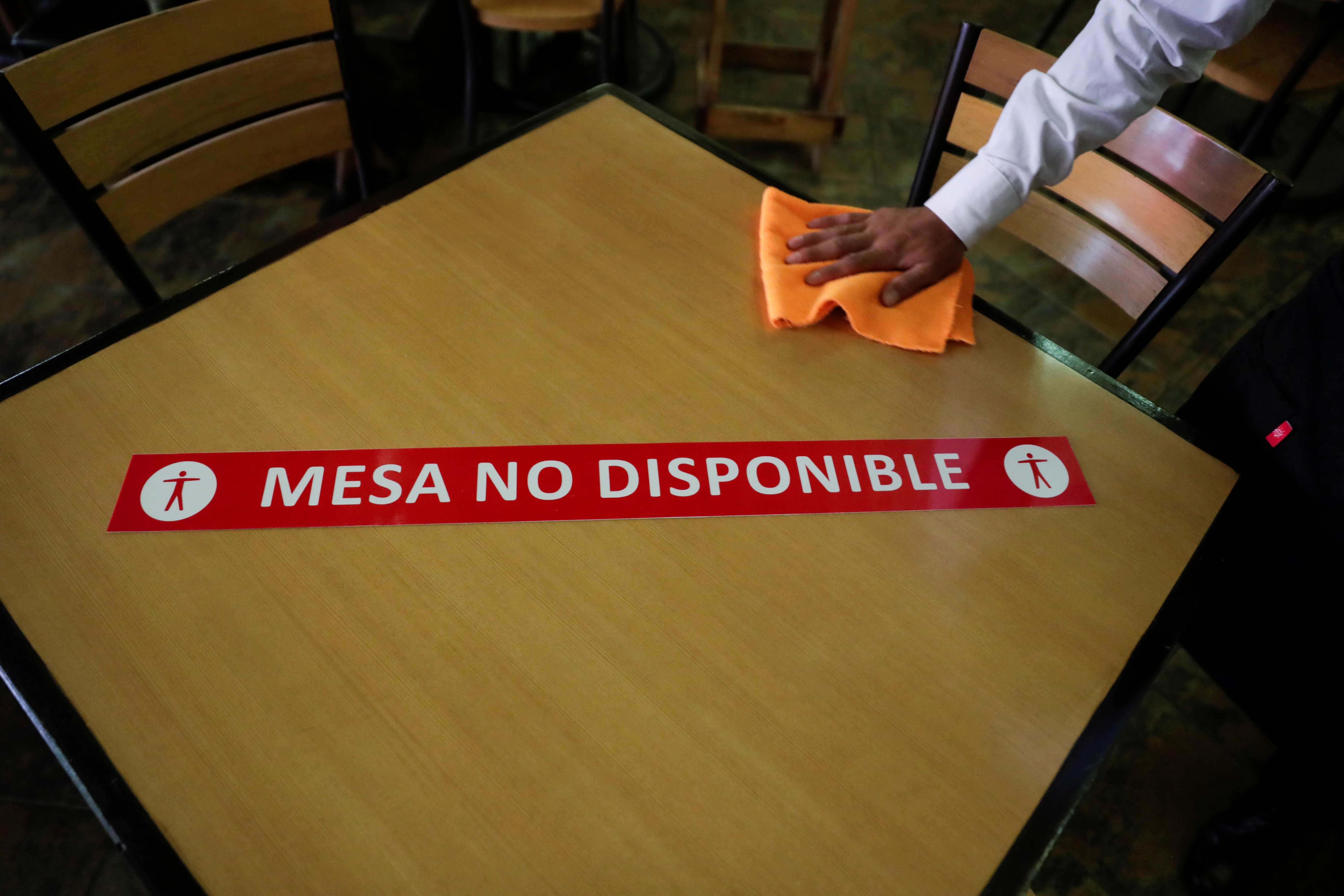 Un camarero limpia una mesa con un cartel de distancia social que dice