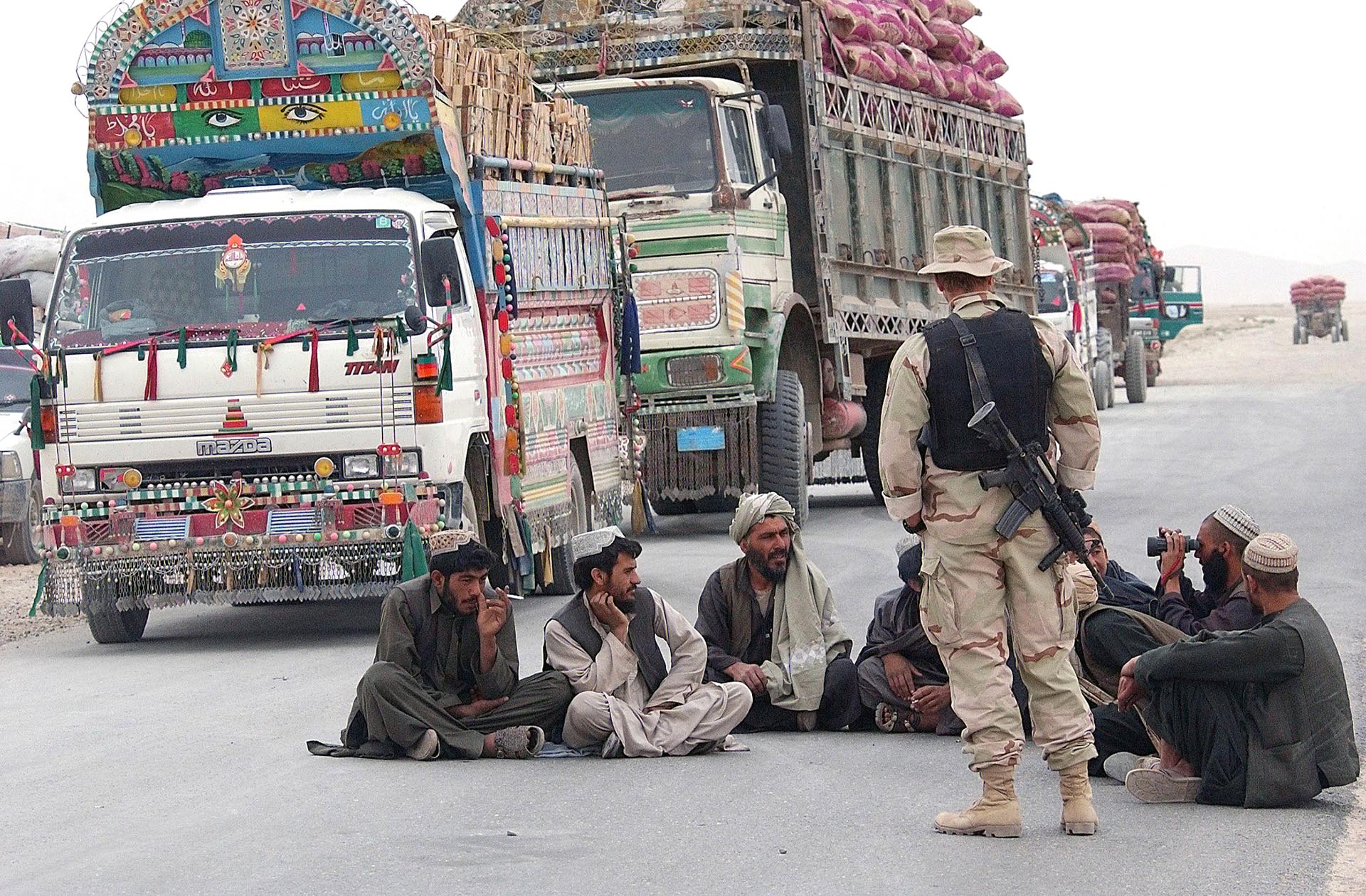 Un soldado del Ejército de los Estados Unidos con hombres afganos mientras esperan a una distancia segura de 3000 libras de bombas detonadas fuera del perímetro de la base aérea de Kandahar. Un afgano usa binoculares para observar la explosión. 13 de abril de 2002. (Everett/Shutterstock)