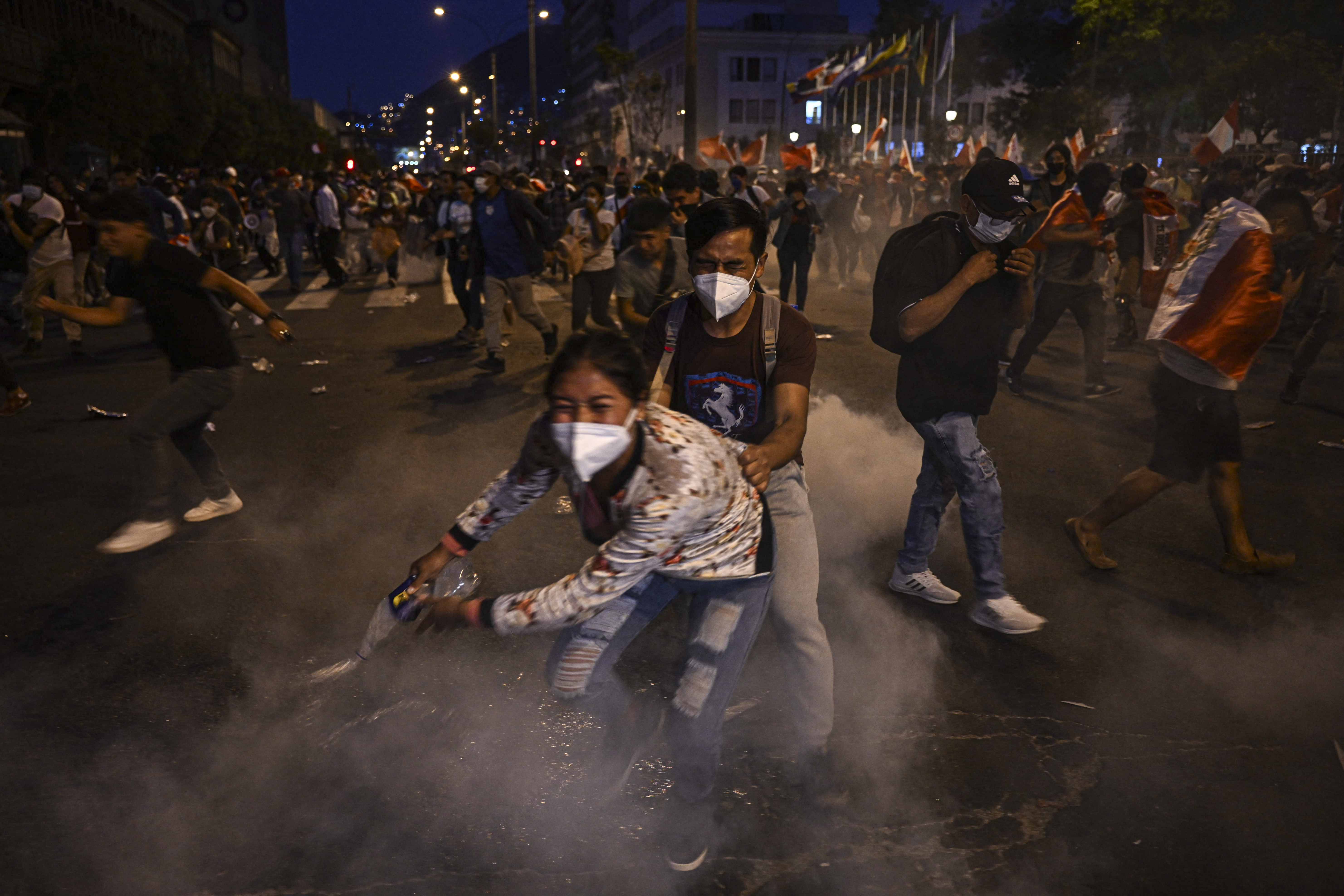 Supporters of former President Pedro Castillo take cover from tear gas thrown by the police during clashes on a demonstration demanding his release and the closure of the Peruvian Congress in Lima, on December 11, 2022. - Two people died and at least five people were injured on Sunday during growing protests against Peru's President Dina Boluarte after the failed coup and the arrest of former President Pedro Castillo. (Photo by ERNESTO BENAVIDES / AFP)