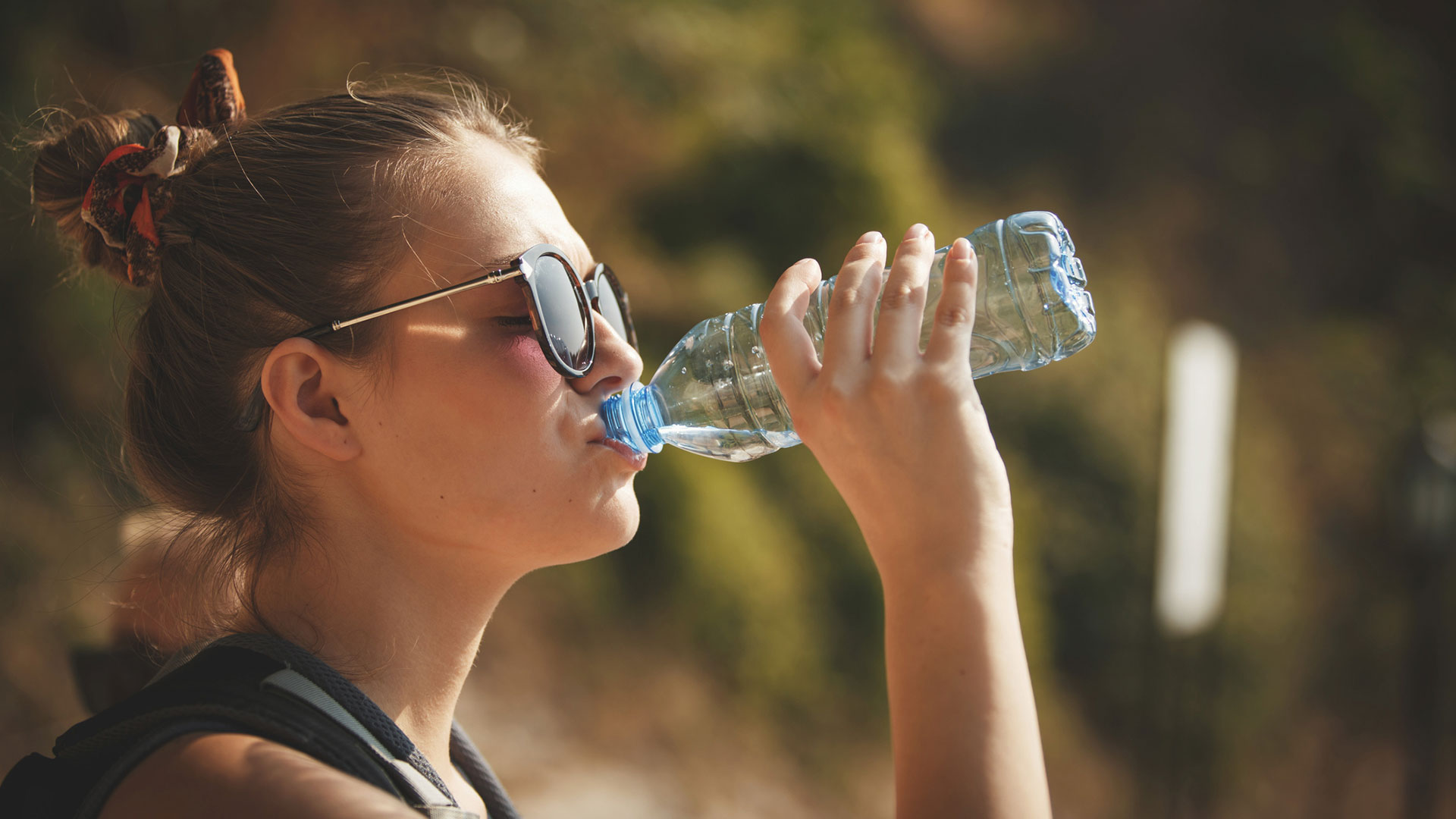 Side view of young woman drinking water from a bottle on a hot summer day.  (getty)