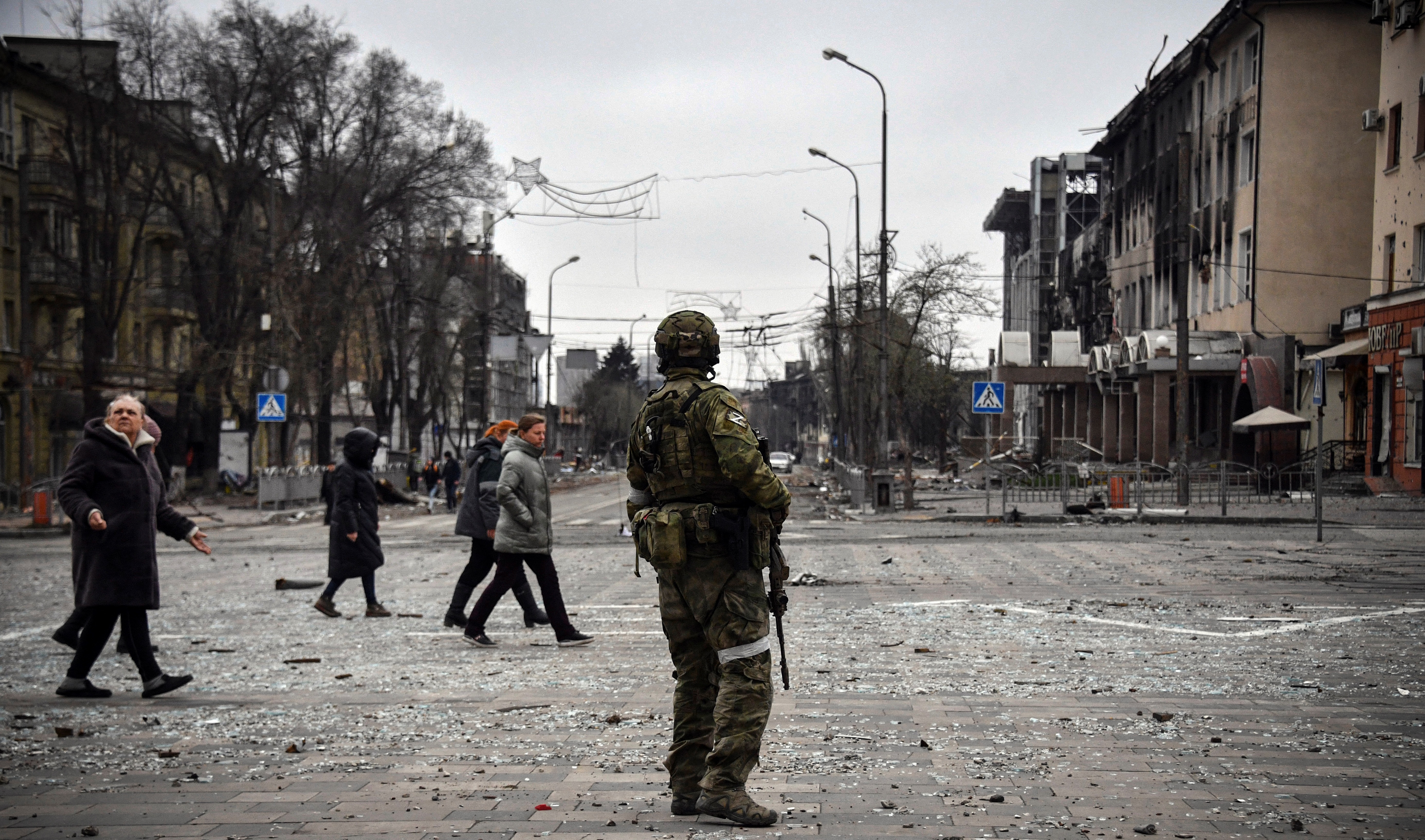 La gente pasa junto a un soldado ruso en el centro de Mariupol el 12 de abril de 2022 (Alexander NEMENOV / AFP)