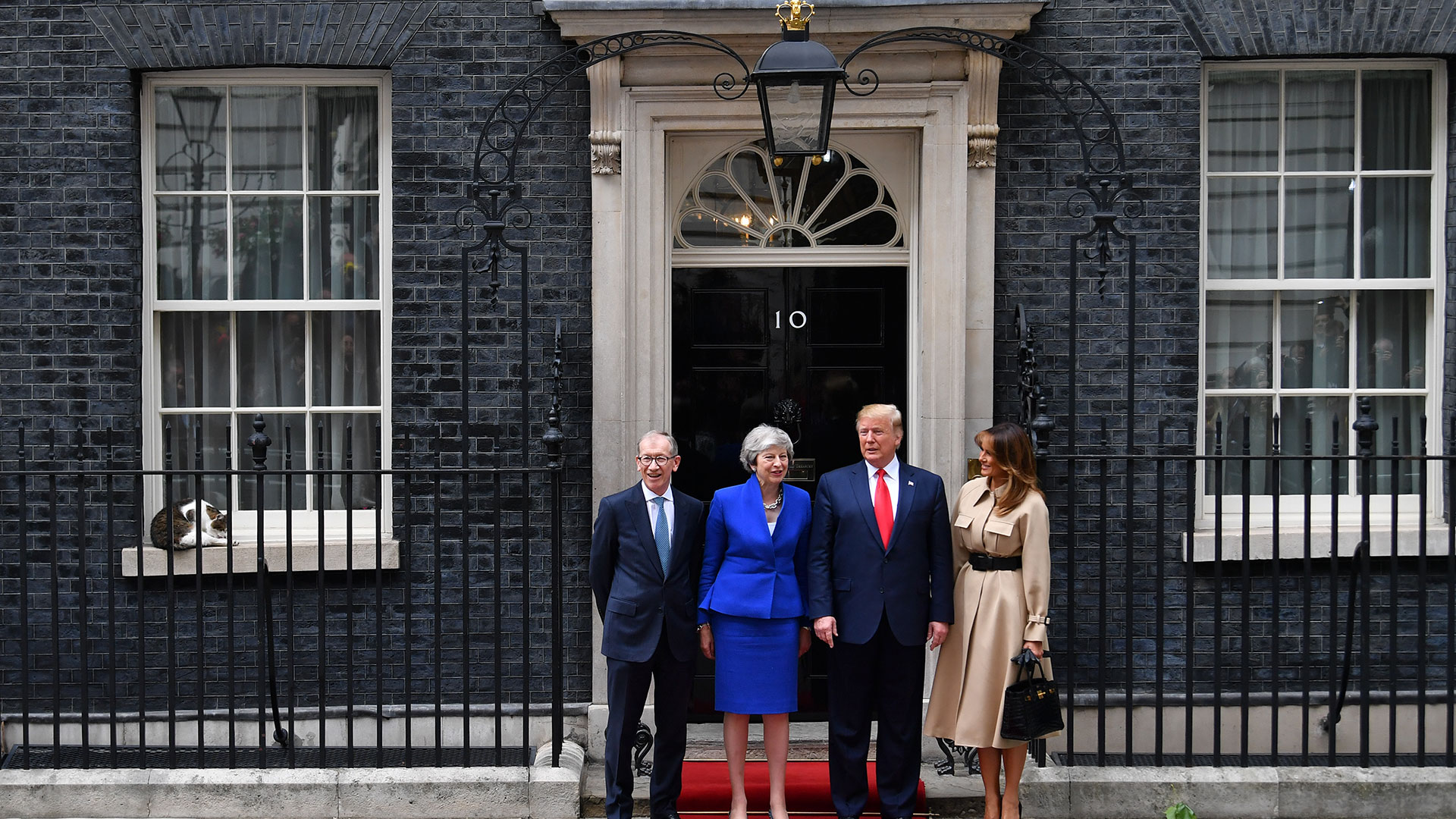 El gato Larry se sienta en el alféizar de la ventana mientras la entonces premier británica Theresa May y su esposo Philip May saludan al entonces presidente estadounidense Donald Trump y a la Primera Dama Melania Trump (Reuters)