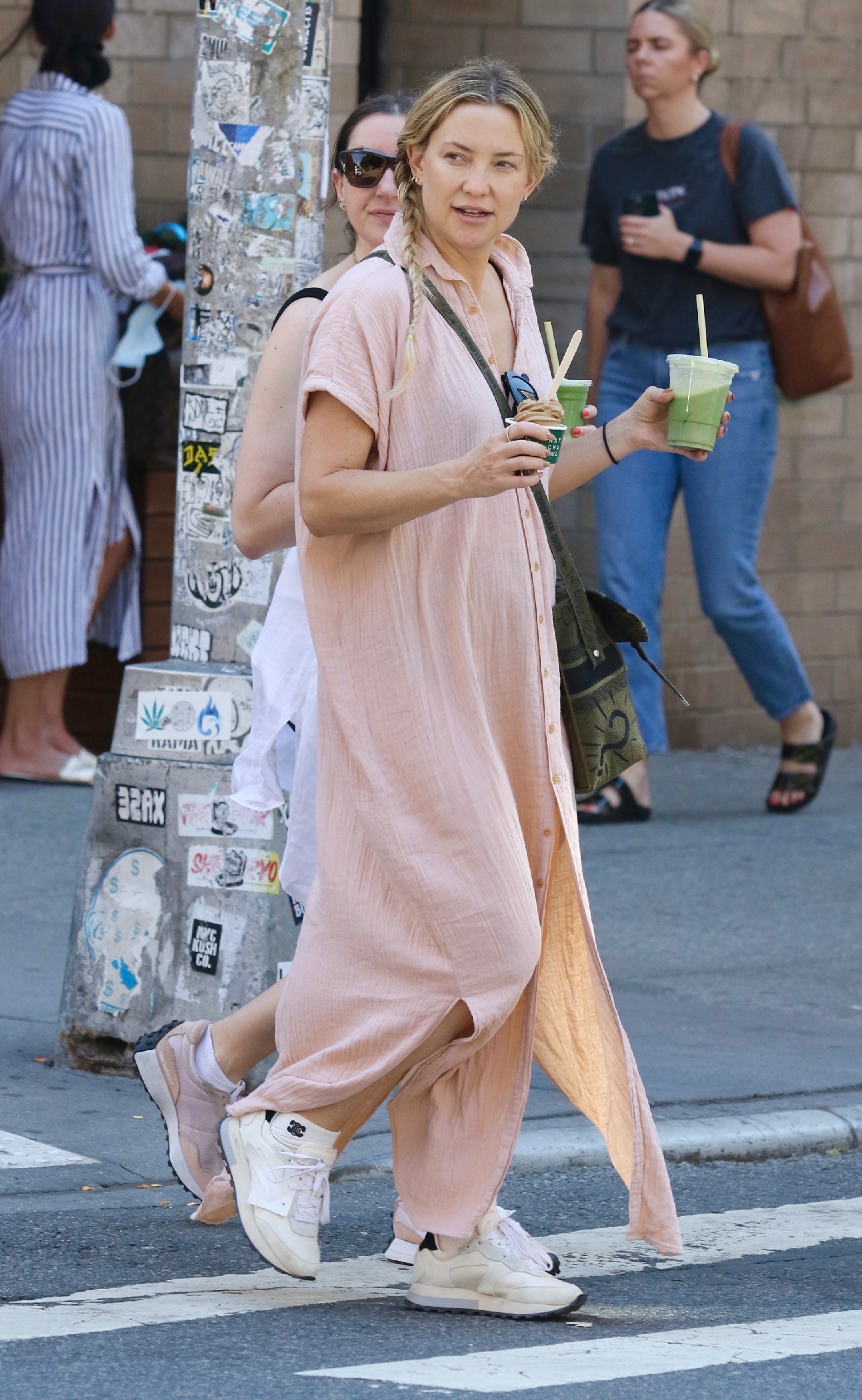Kate Hudson took a walk through the streets of the Soho neighborhood in New York, accompanied by a friend, with whom she stopped to buy a juice to go.  She wore a long pink dress with buttons and short sleeves.  She also wore comfortable sneakers, sunglasses and a shoulder bag.