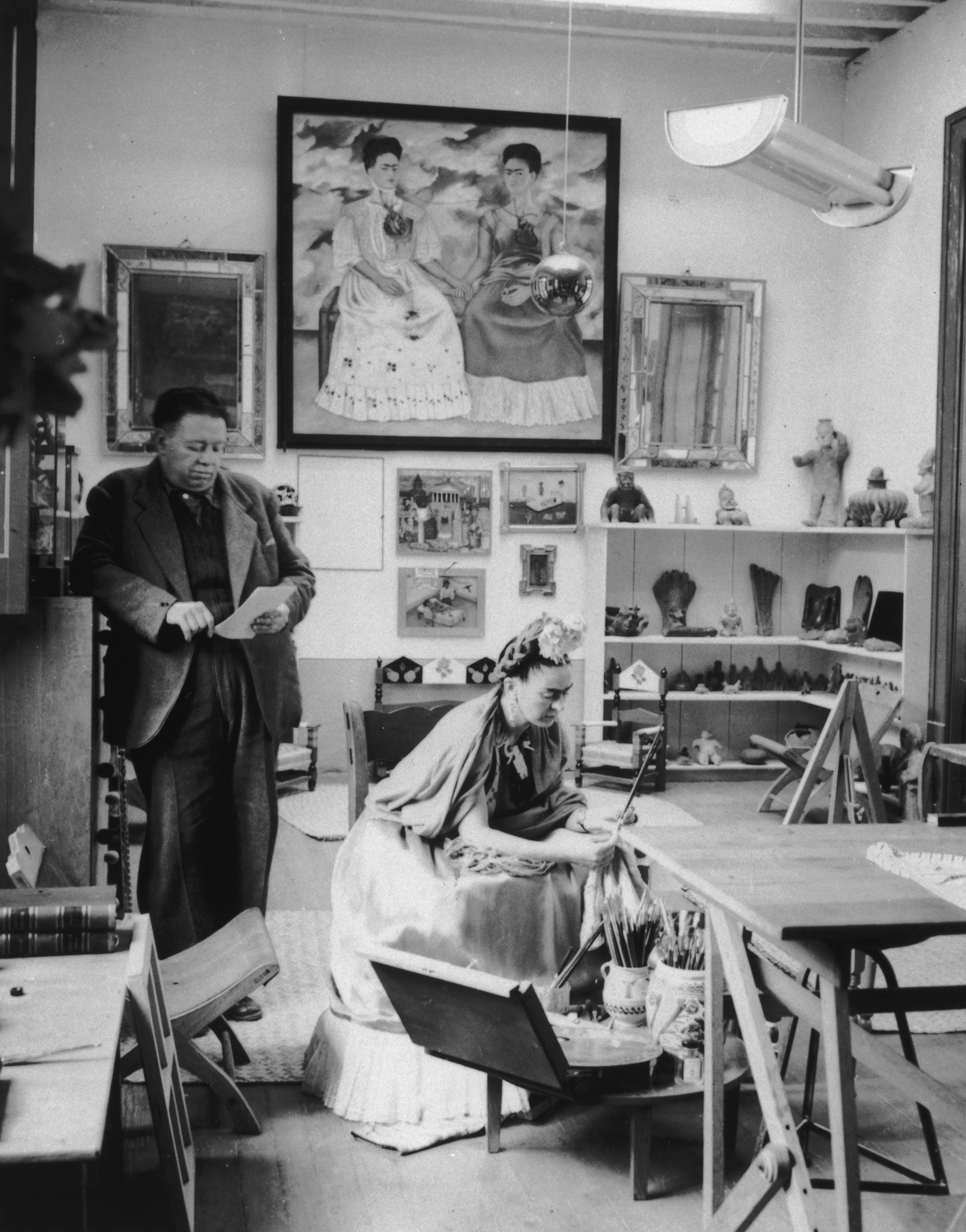 ​​Rivera y Kahlo leen y trabajan en un estudio en 1945. El autorretrato de Kahlo, 'Las dos Fridas' (1939),  que se encuentra en el mexicano Museo de Arte Antiguo, cuelga de fondo con otras obras (Hulton Archive / Getty Images)