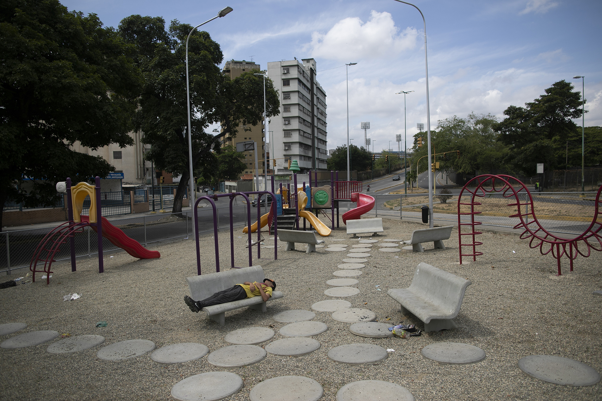 Un hombre duerme en un banco de un parque de juegos vacío en plena cuarentena para combatir la propagación del coronavirus, en Caracas, Venezuela, el 7 de abril de 2020. (AP Foto/Ariana Cubillos)