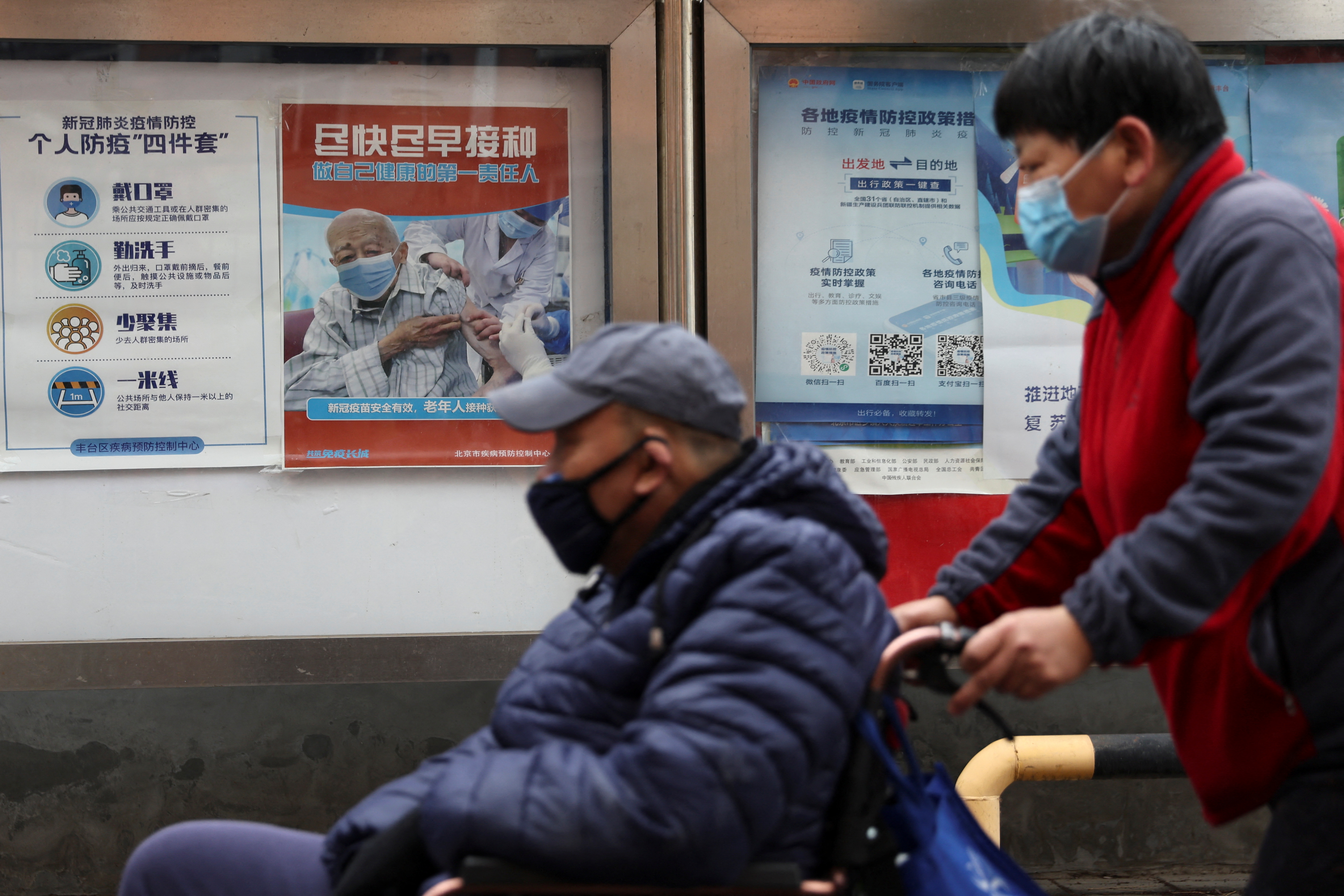 Mientras un anciano pasa asistido para su desplazamiento en Beijing, el afiche del fondo insta a los mayores chinos a vacunarse (REUTERS/Tingshu Wang)