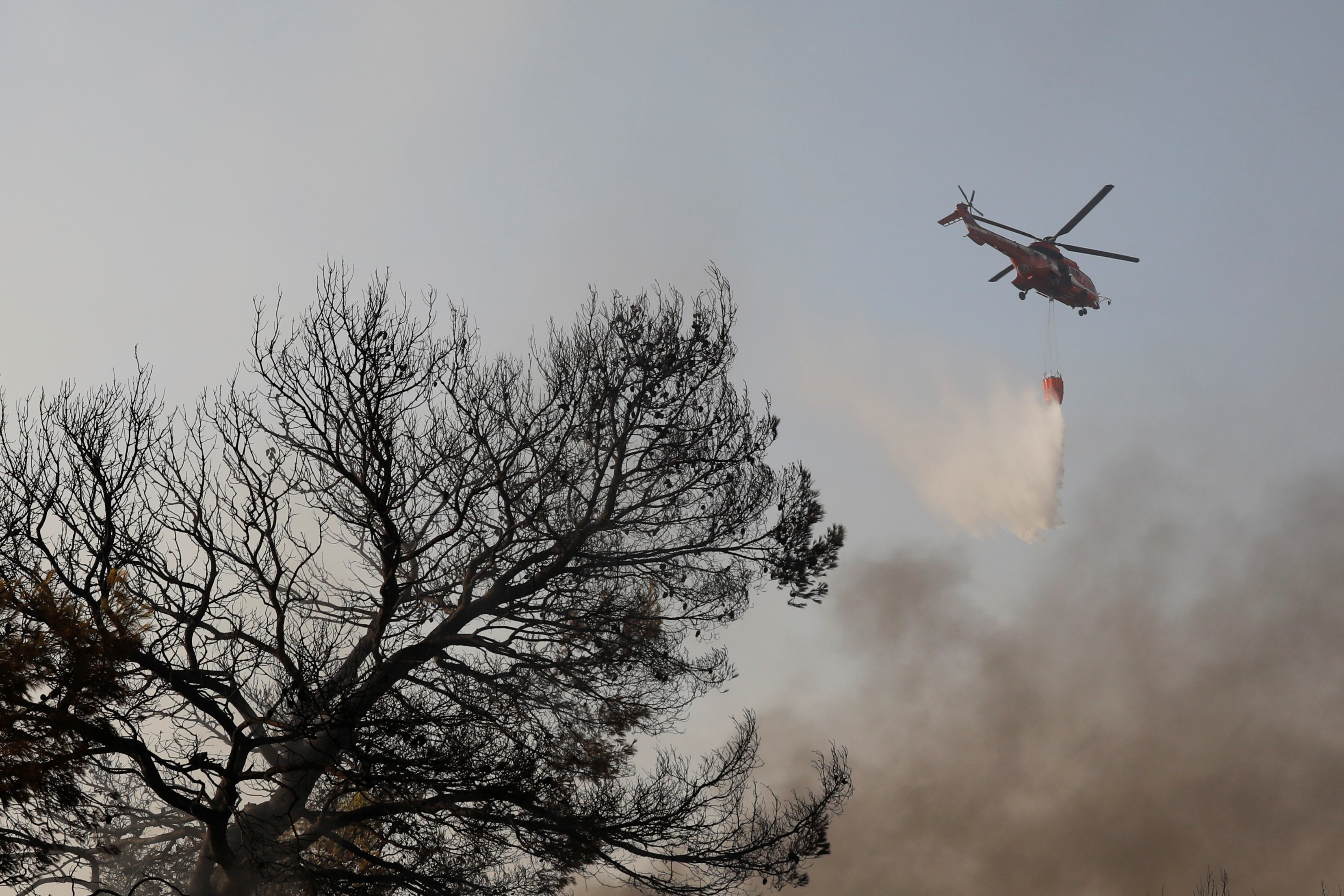 Un helicóptero de extinción de incendios hace una gota de agua mientras un incendio forestal arde en el suburbio de Varympompi al norte de Atenas, Grecia, el 4 de agosto de 2021. REUTERS / Costas Baltas
