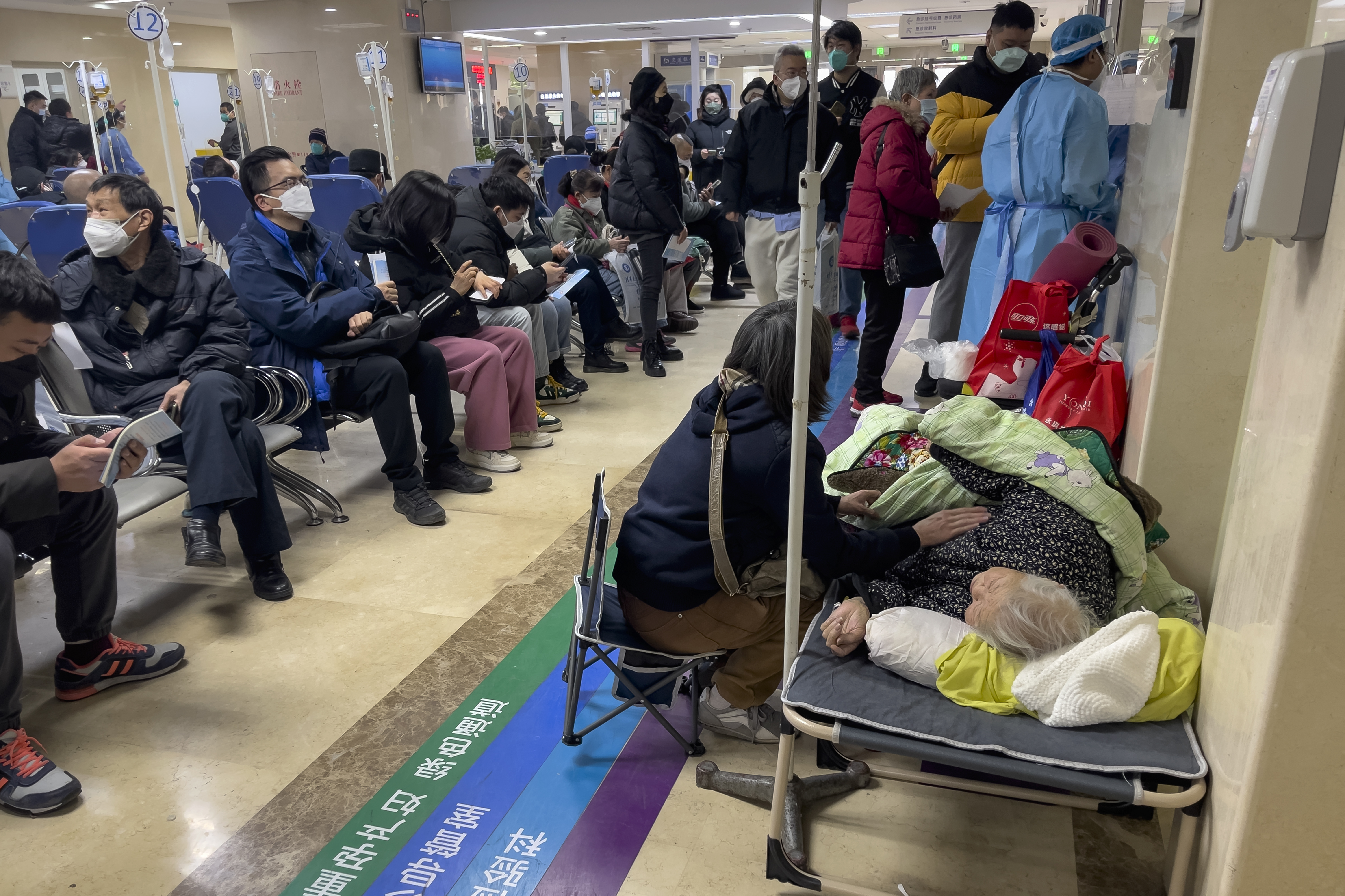 Una mujer cuida a un familiar mayor tendido en una camilla mientras recibe tratamiento intravenoso en una sala de emergencias atestada de un hospital de Beijing