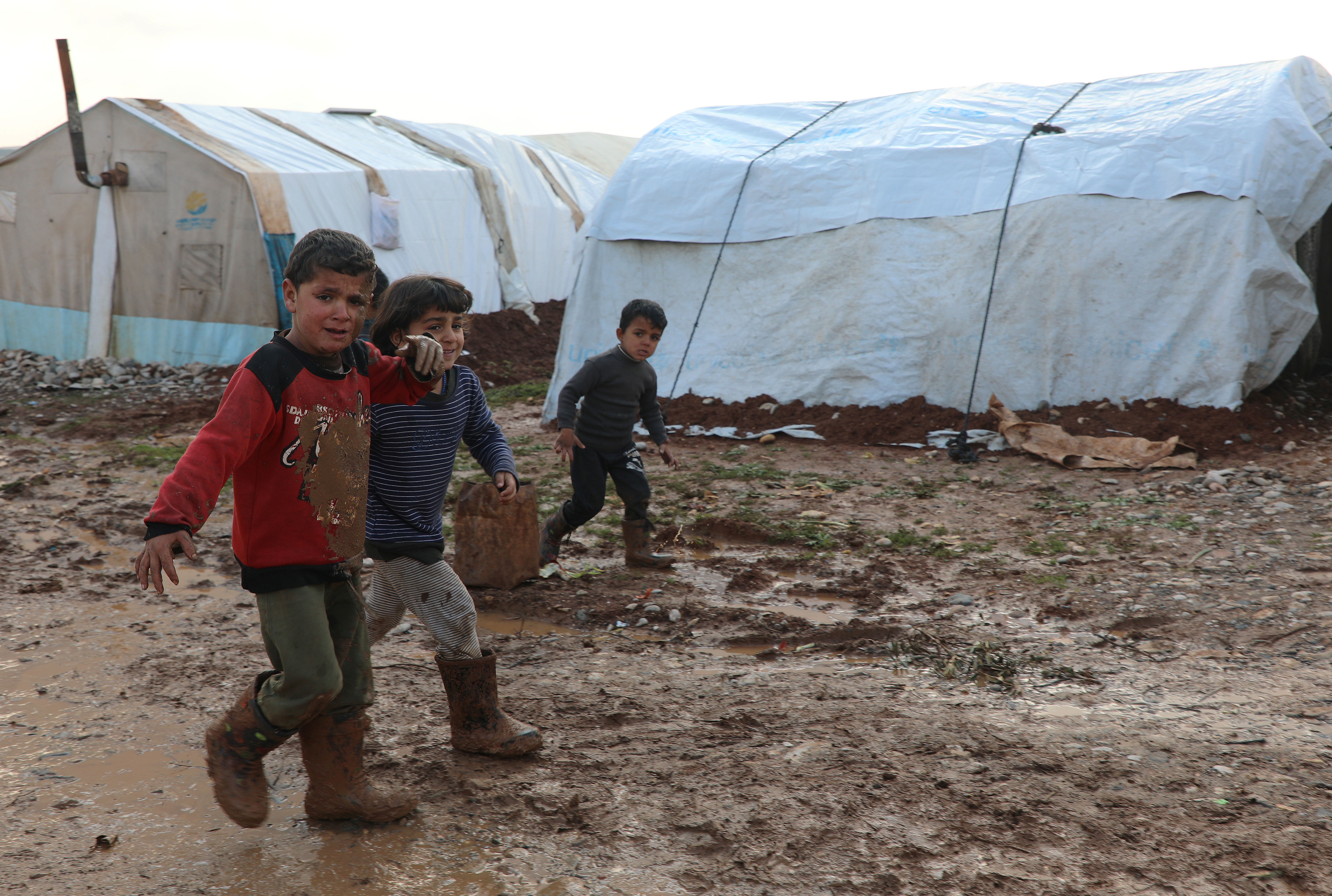 Niños sirios desplazados internos caminan en el barro cerca de las tiendas de campaña, en el campo del norte de Alepo, Siria, 20 de enero de 2021. Fotografía tomada el 20 de enero de 2021. REUTERS / Mahmoud Hassano
