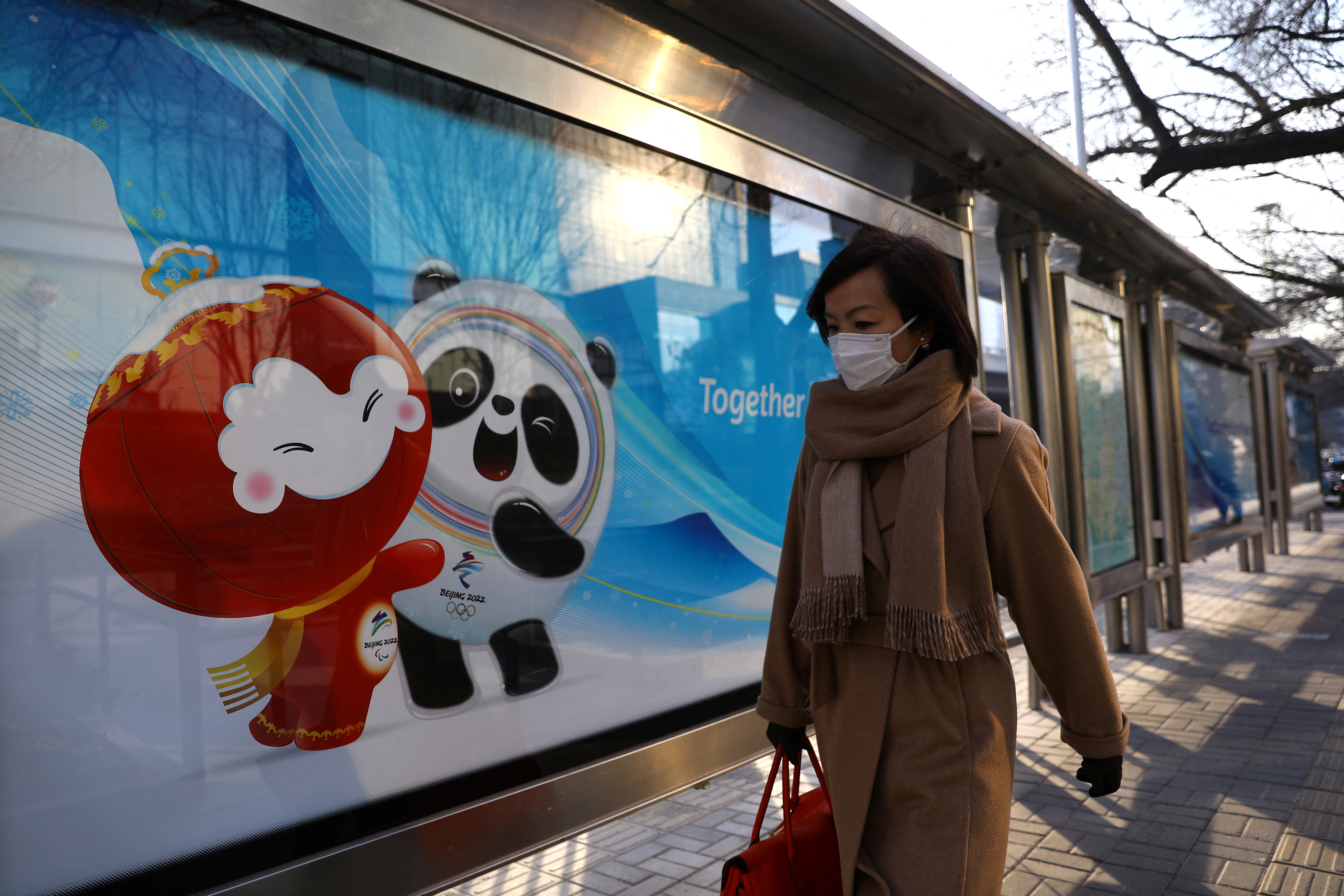 A woman walks past a board with an image of the Beijing 2022 Winter Olympics mascots at a bus stop in Beijing, China January 18, 2022. REUTERS/Tingshu Wang