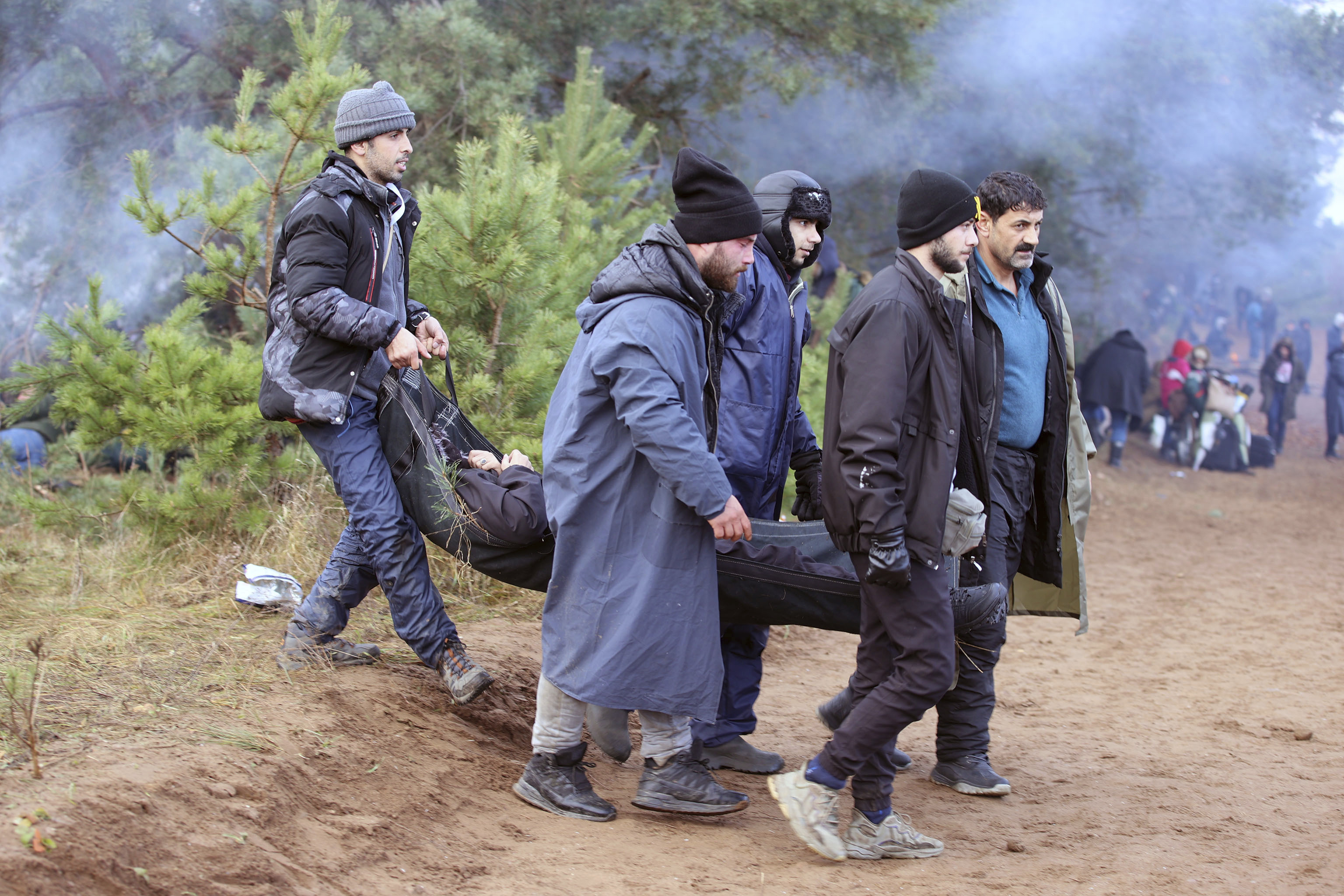 Un grupo de migrantes cargan con su amigo enfermo cerca de la frontera (Leonid Shcheglov/BelTA via AP)