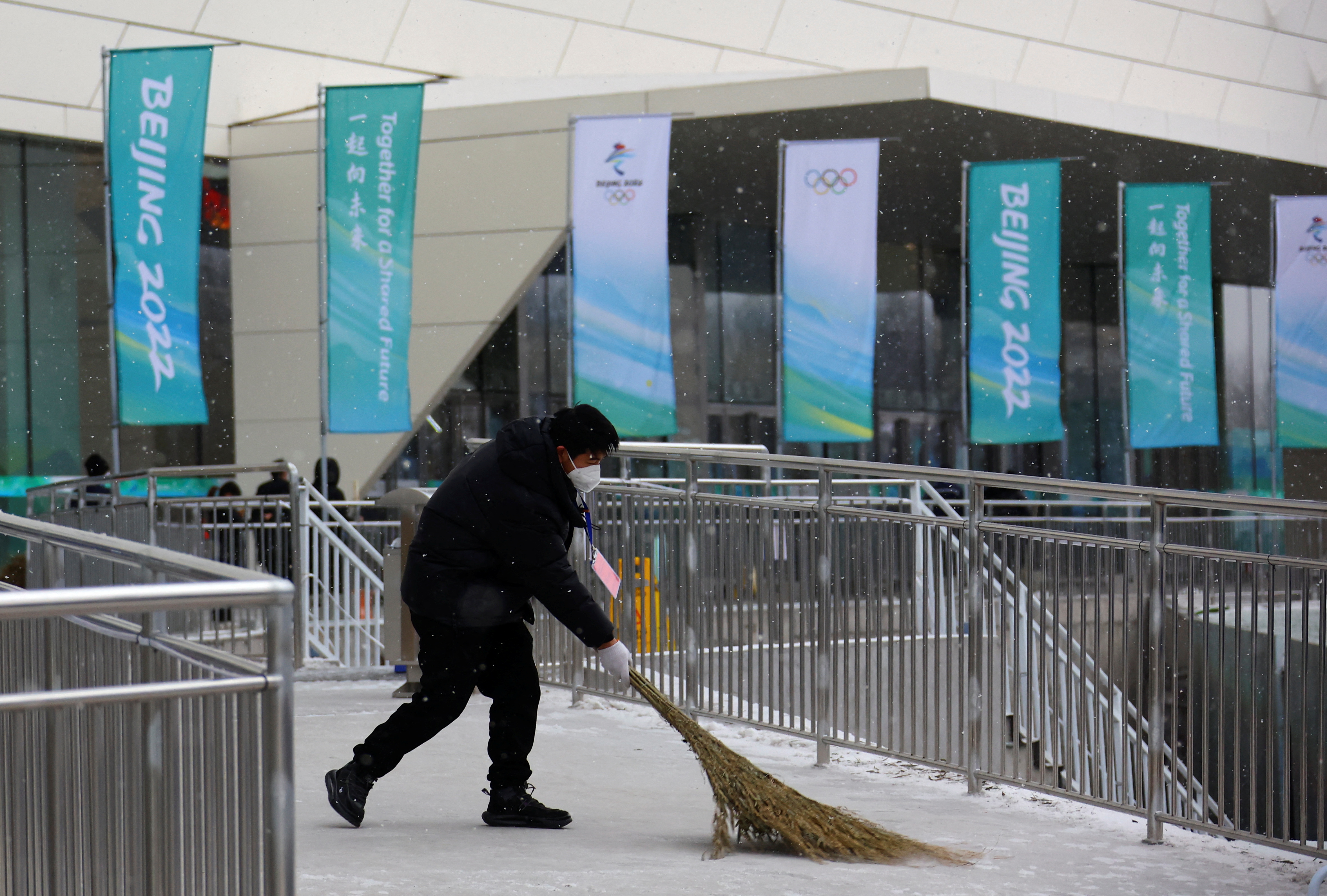 A worker cleans a street during snowfall outside the Main Press Centre ahead of the Beijing 2022 Winter Olympics in Beijing, China January 20, 2022. REUTERS/Fabrizio Bensch