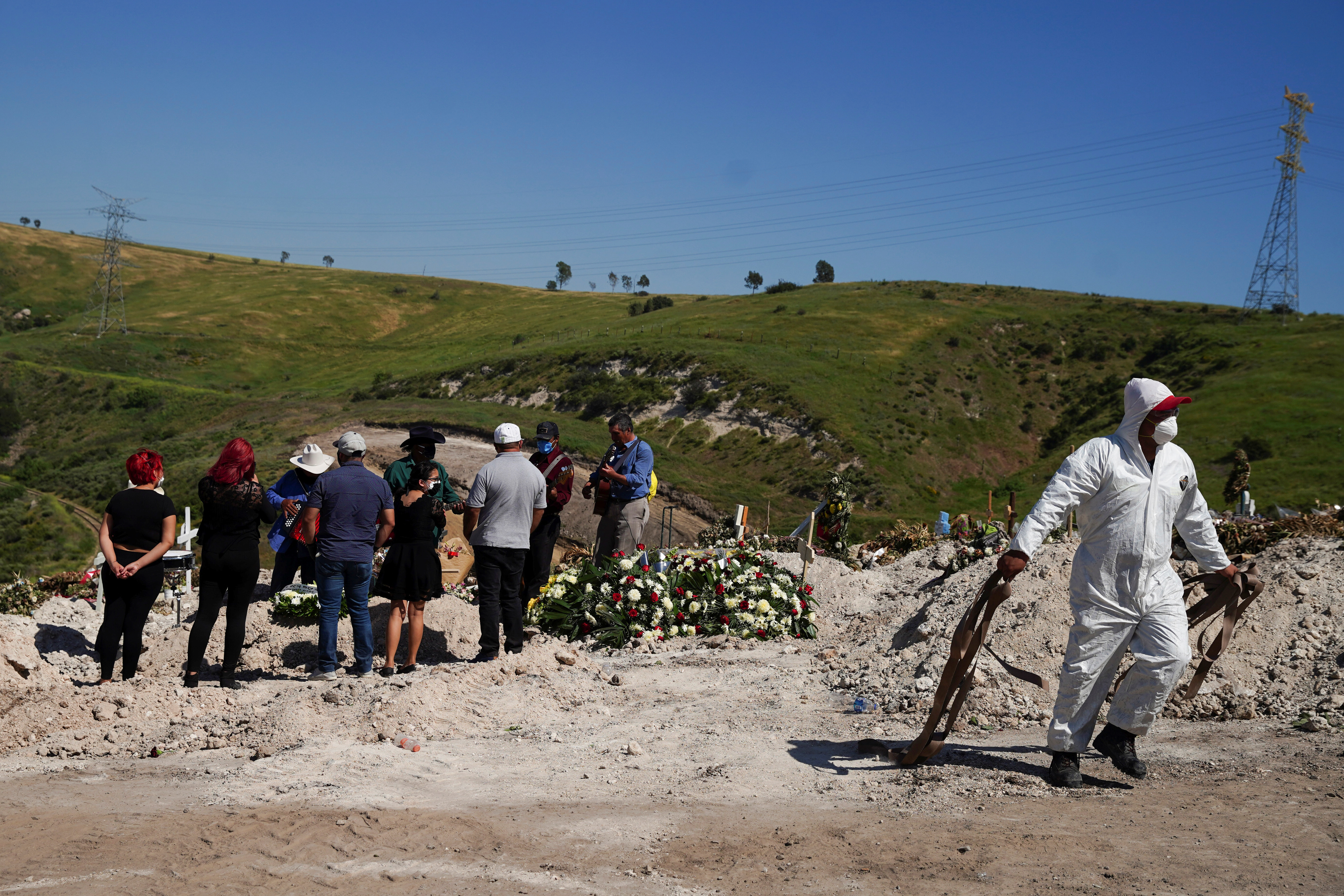 Un trabajador en traje protector camina con las correas usadas para bajar el ataúd a la tumba para el entierro de Jesús Osorio Flores, quien murió de coronavirus en el Cementerio Municipal de Tijuana No. 13, en Tijuana, México, el 24 de abril de 2020 (REUTERS/Ariana Drehsler)