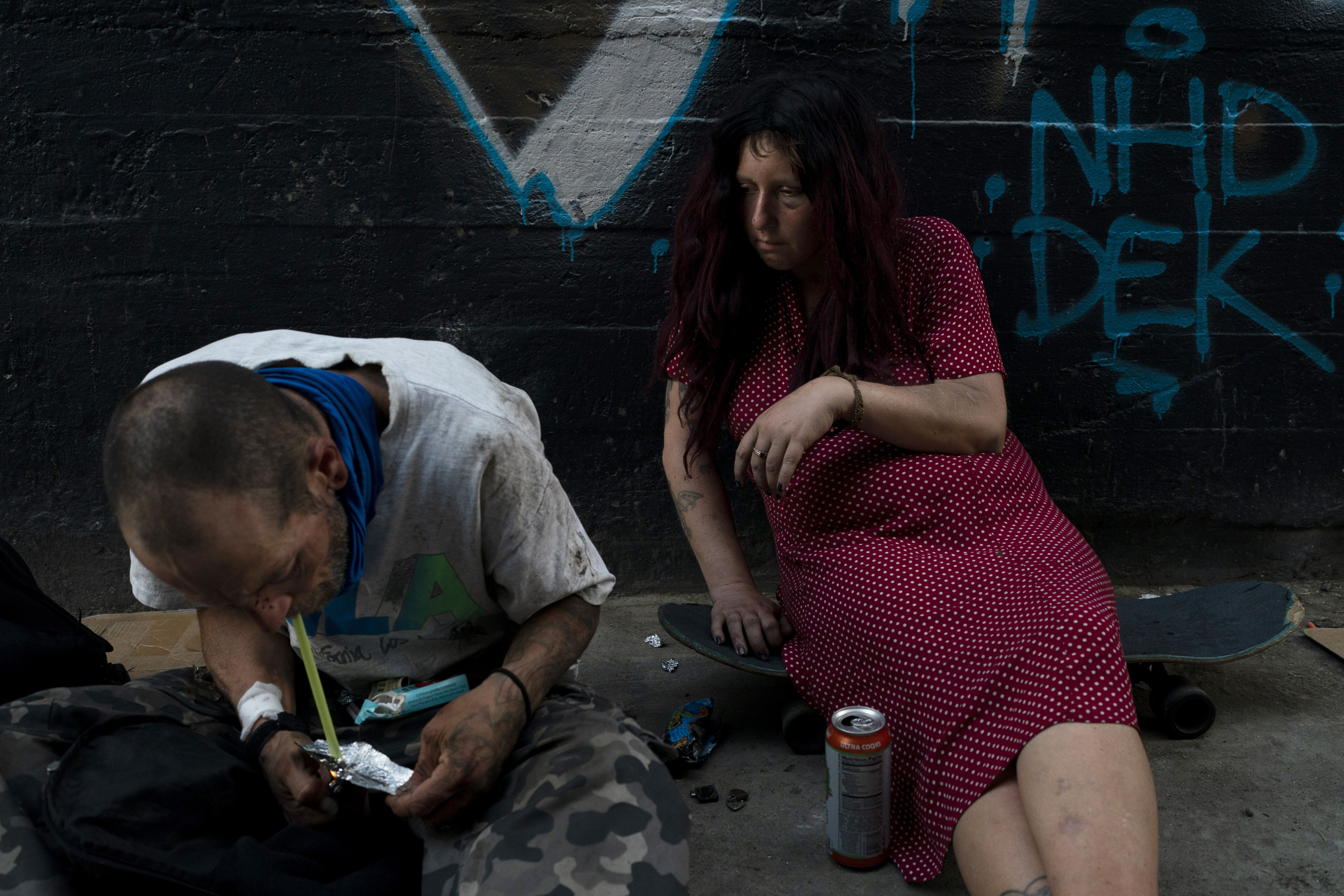 Jenn Bennett, who is high on fentanyl, sits on her skateboard with a black eye as her friend, Jesse Williams, smokes the drug on Tuesday, Aug. 9, 2022, in Los Angeles.  (AP Photo/Jae C. Hong)