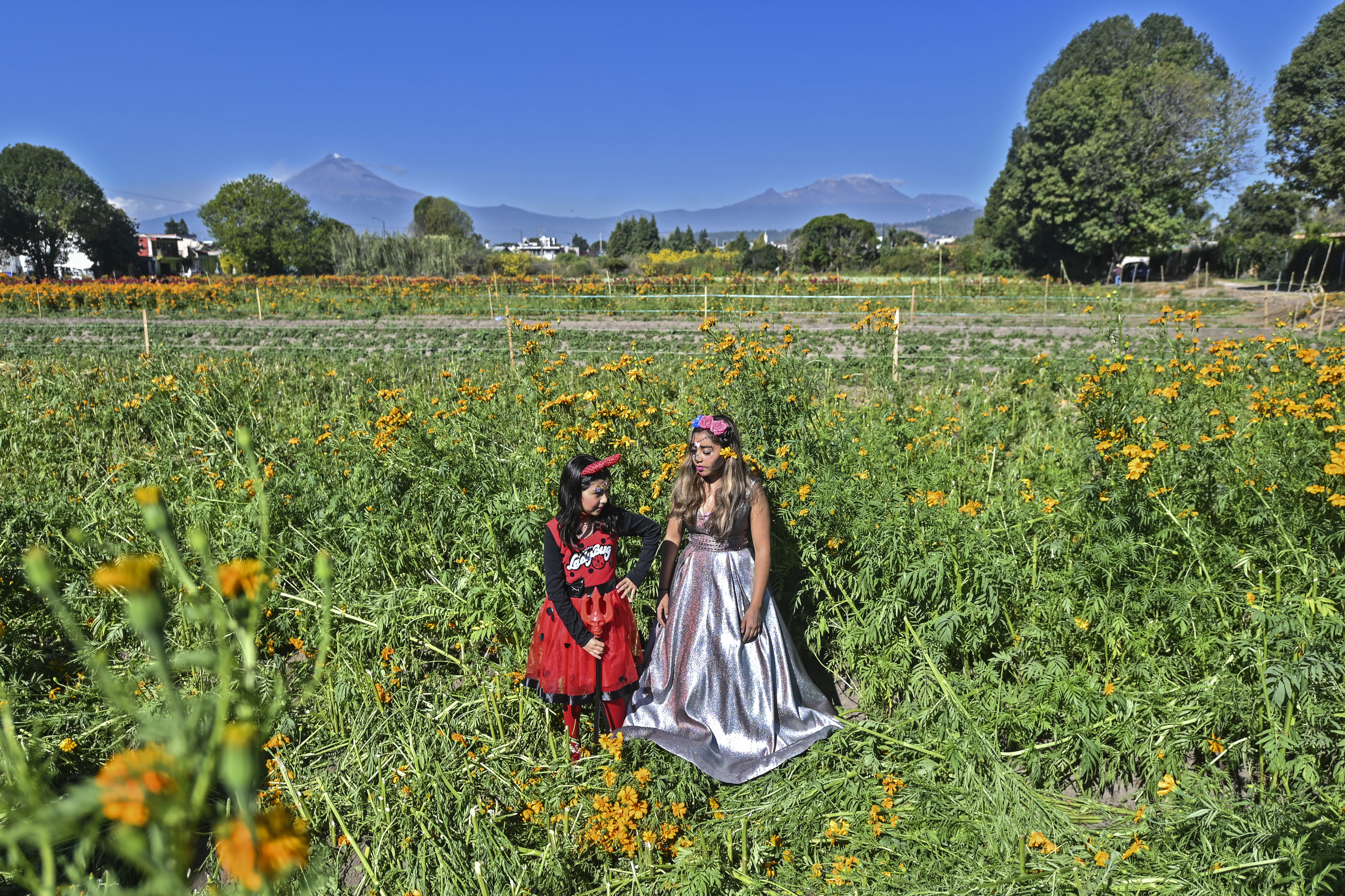 Niñas disfrazadas de Catrina y un diablo respectivamente, posan en un campo de cultivo en San Pedro Cholula, estado de Puebla, México, el 1 de noviembre de 2020.