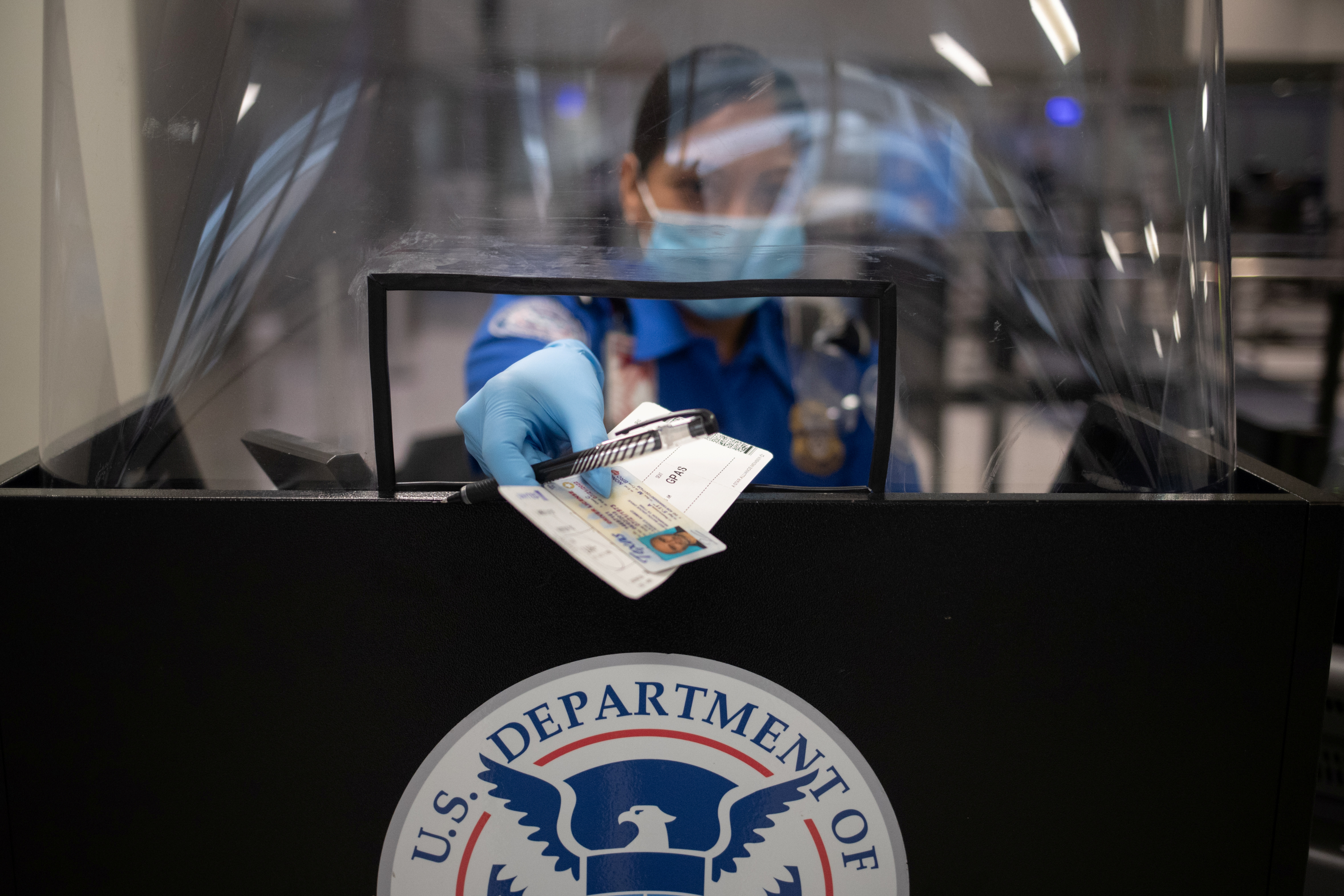 Una empleada de la TSA devuelve los documentos a un pasajero, ahora con barbijo y cobertor plástico producto del coronavirus. REUTERS/Adrees Latif