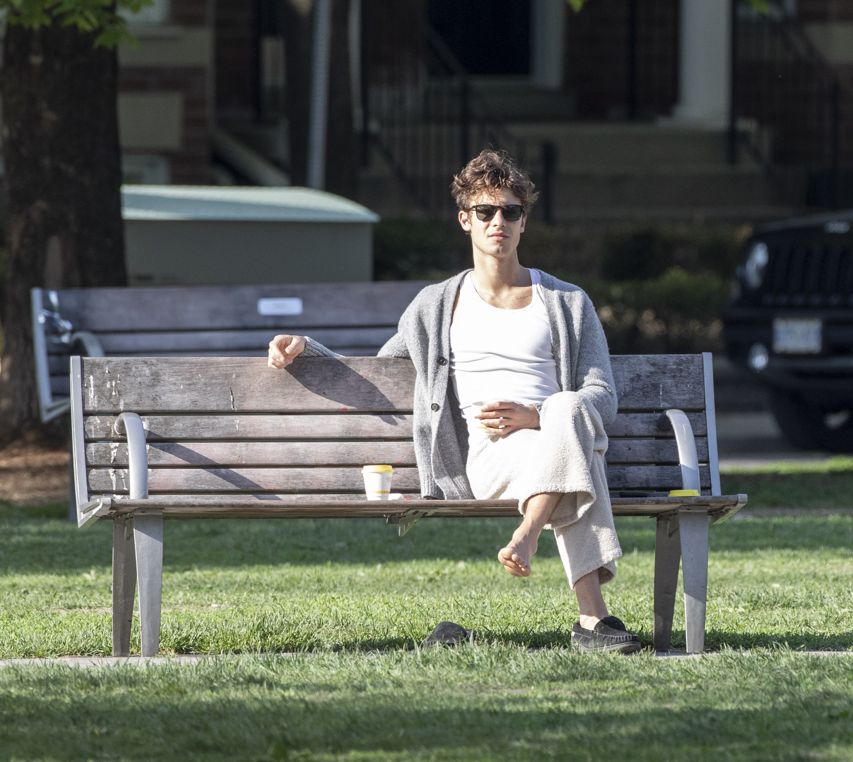 Shawn Mendes enjoyed a day outdoors in a park in Toronto, Canada.  The artist sat on a bench to wait for a friend he met.  He wore white faux lambskin pants, a classic t-shirt and a gray wool sweater.
