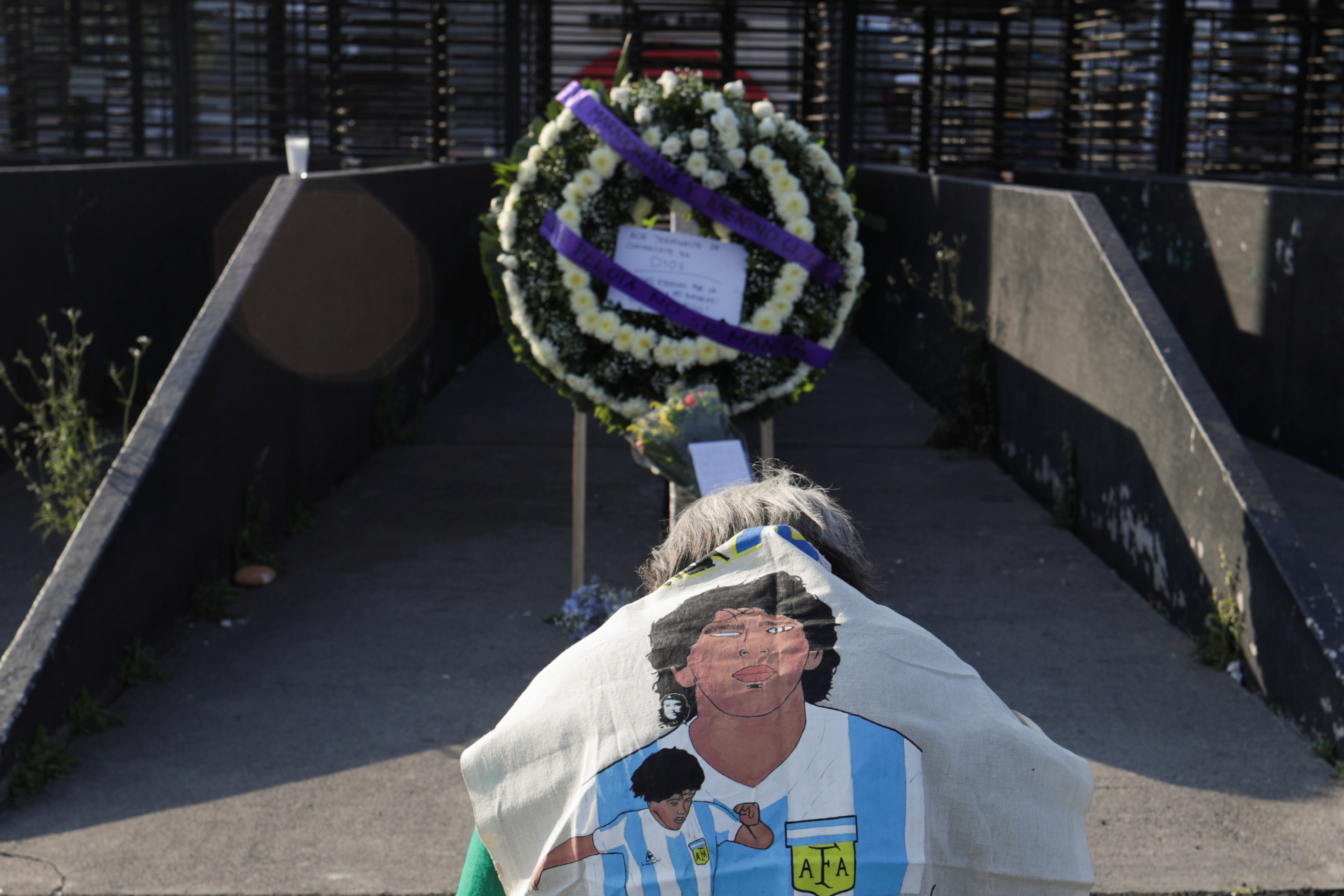 Un fanático se arrodilla mientras coloca una imagen de la leyenda del fútbol argentino Diego Armando Maradona junto a una ofrenda floral en su memoria afuera del estadio Azteca, en la Ciudad de México, México, 26 de noviembre de 2020.