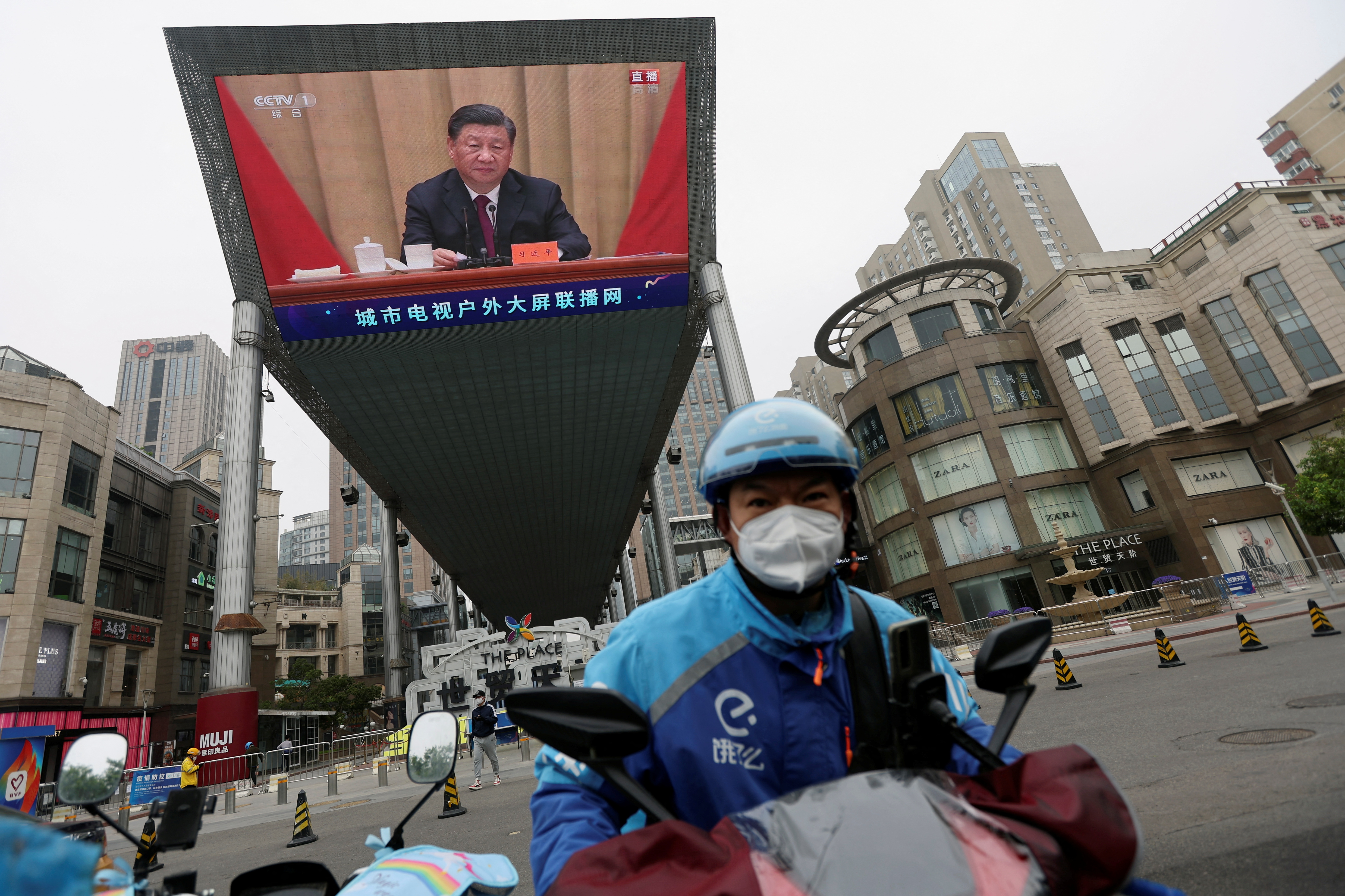 Un repartidor de Ele.me conduce su motocicleta cerca de una pantalla gigante que muestra al jefe del régimen chino Xi Jinping en un acto de celebración del centenario de la fundación de la Liga de la Juventud Comunista China, en Beijing (Reuters)