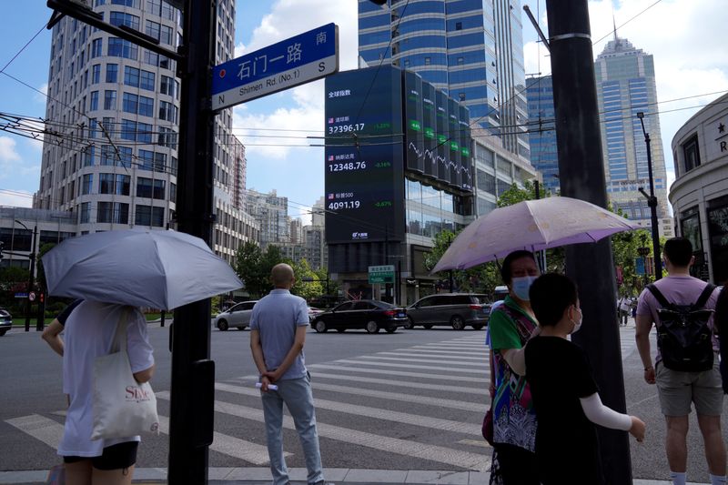 File image of pedestrians waiting to cross a street on a corner near a giant screen showing stock indices in Shanghai, China.  August 3, 2022. REUTERS/Aly Song/File