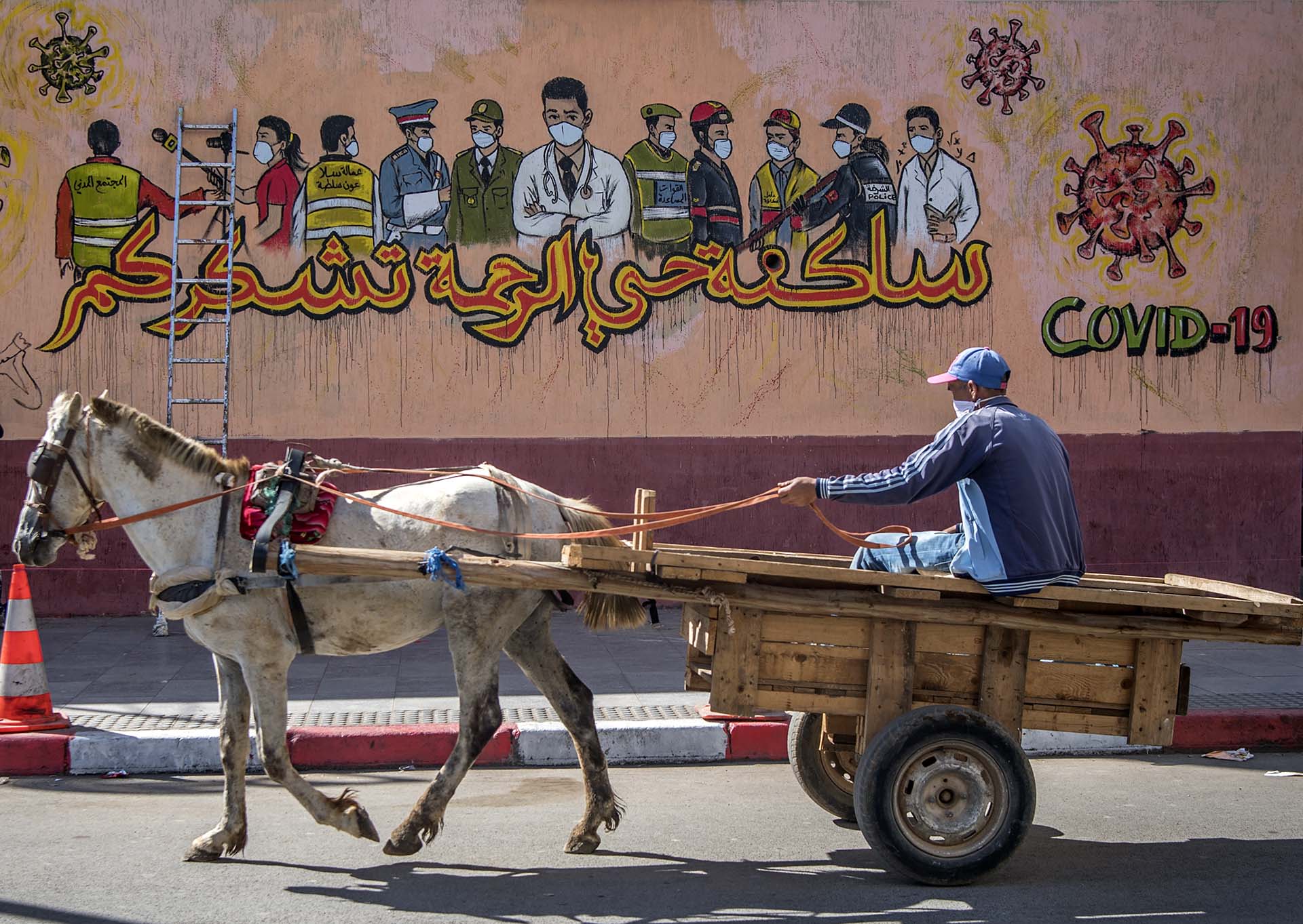 Un hombre pasa con su carro tirado por un caballo frente a un mural pintado en una pared de Sale, cerca de la capital de Marruecos.