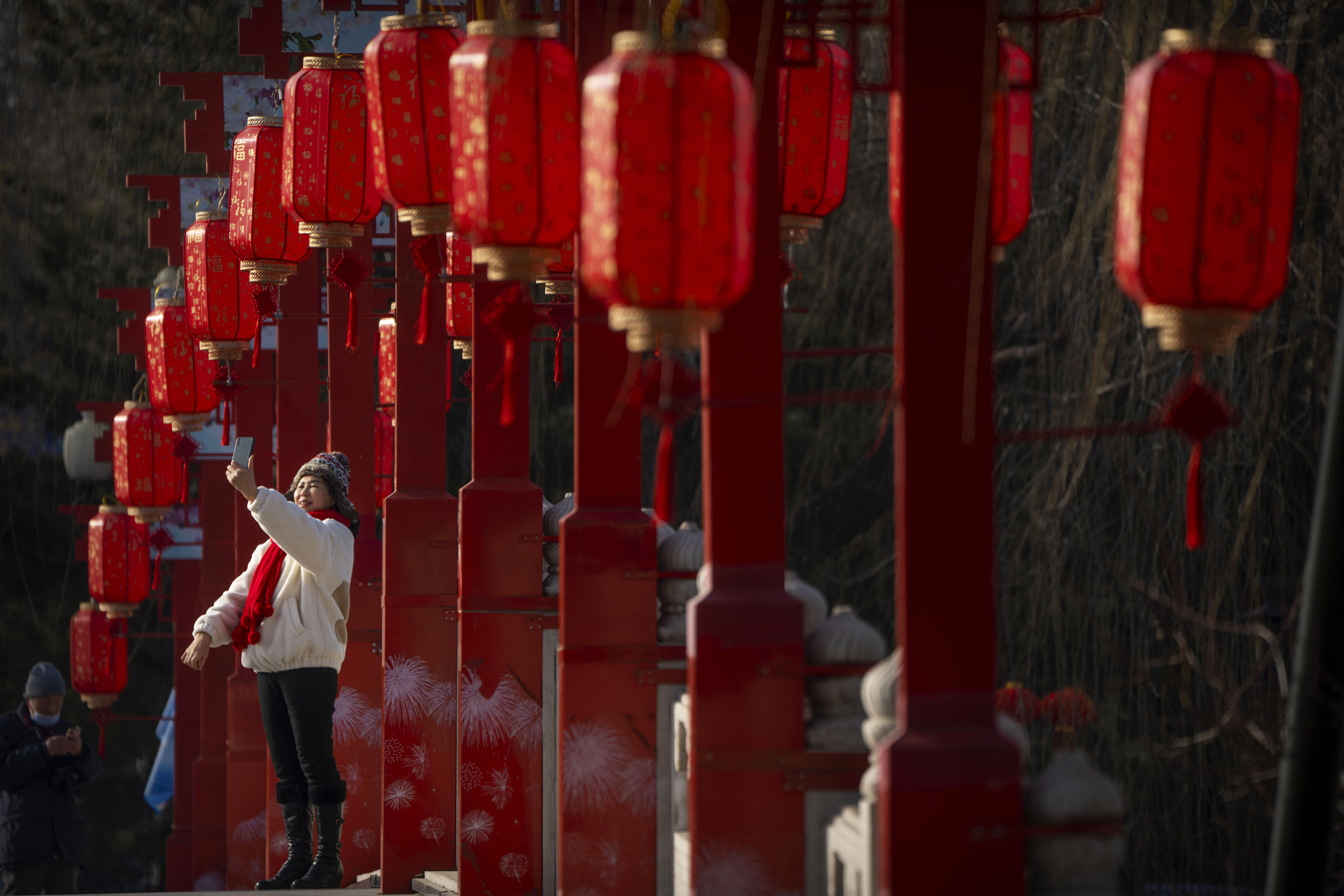 Una mujer se toma una selfie en un puente decorado con linternas en un parque pública en Beijing en el primer día de la fiesta del Año Nuevo Lunar, el domingo 22 de enero de 2023. (AP Foto/Mark Schiefelbein)