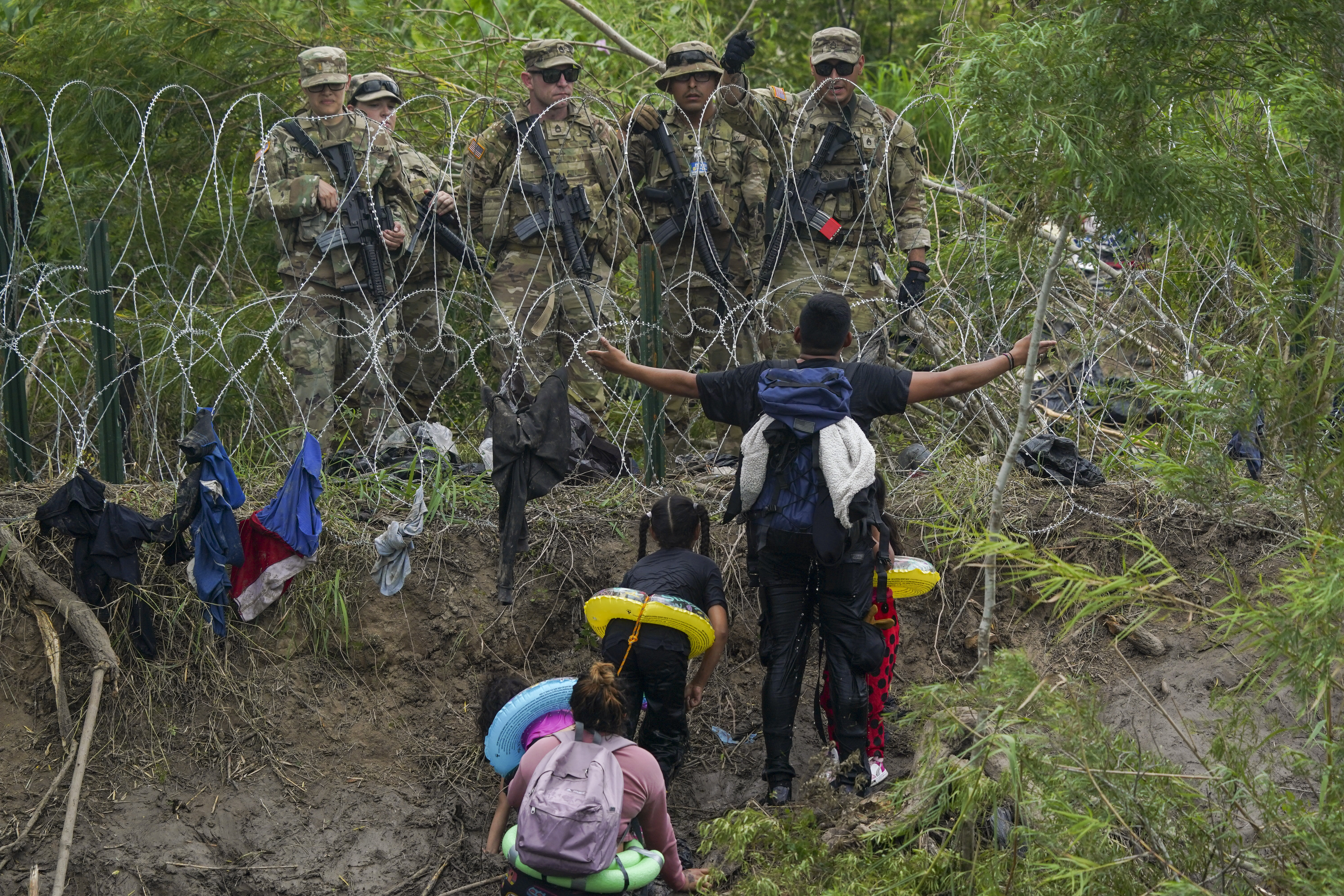 A migrant gestures toward Texas National Guard agents watching from behind barbed wire, on the banks of the Rio Grande, as seen from Matamoros, Mexico, on May 11, 2023. US President Joe Biden's administration has introduced stricter measures to replace Title 42, which since March 2020 has allowed border authorities to quickly expel migrants across the border to prevent the spread of COVID-19.  (AP Photo/Fernando Llano)