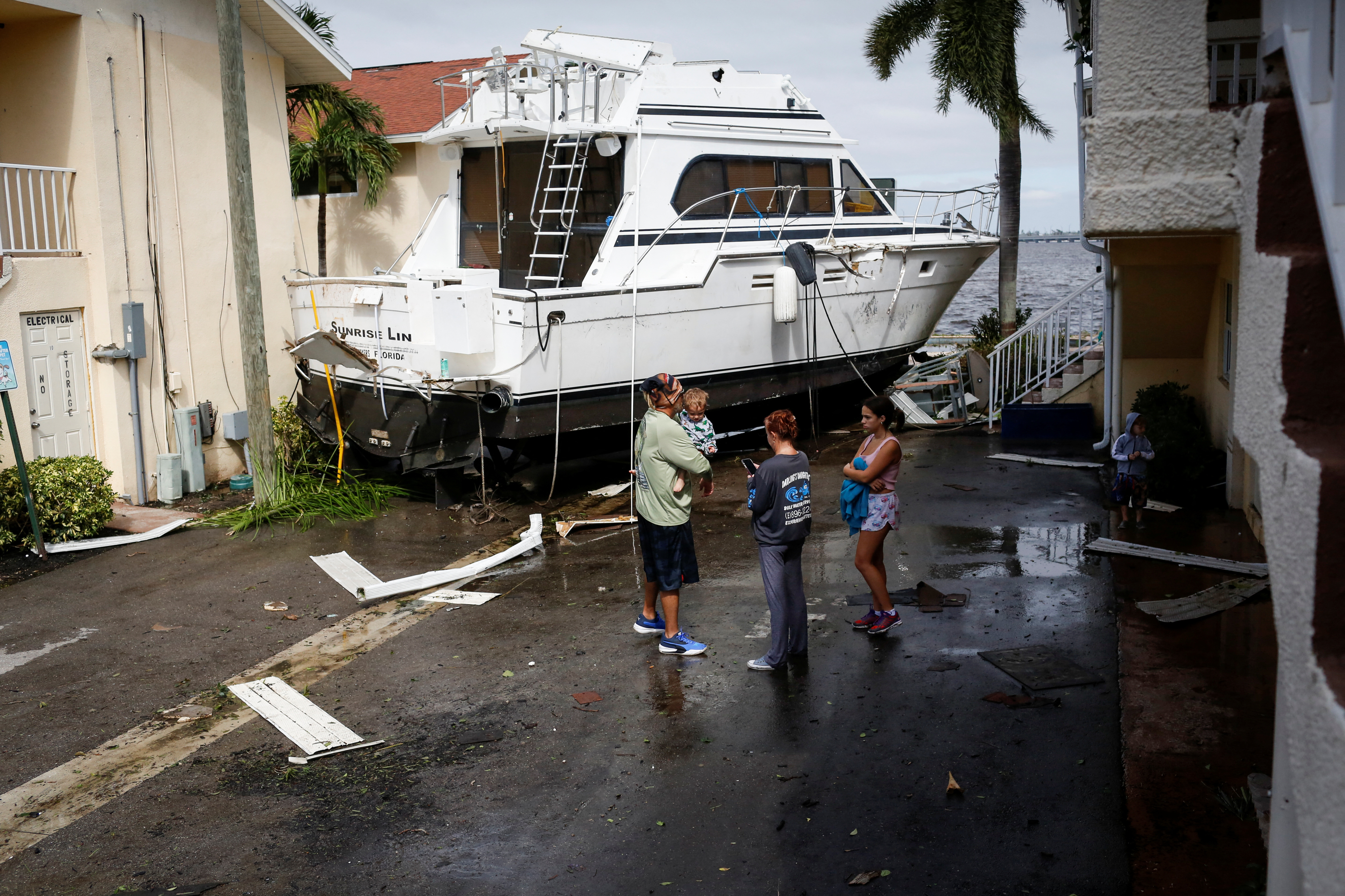 Una familia junto a un bote dañado en medio de un condominio en el centro de la ciudad después de que el huracán Ian causara una destrucción generalizada en Fort Myers, Florida, el 29 de septiembre de 2022. (REUTERS/Marco Bello)