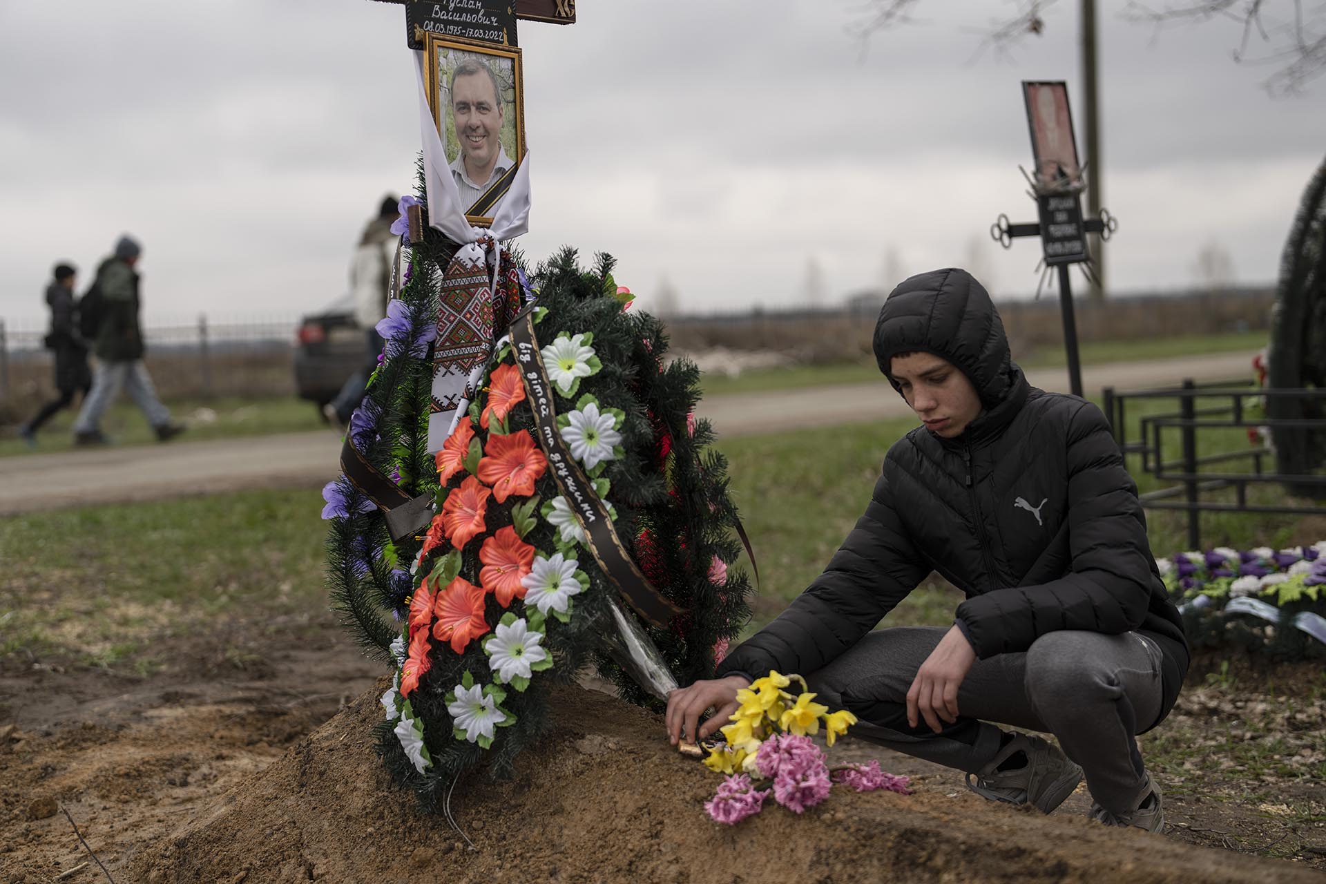 Yura Nechyporenko coloca una chocolatina en la tumba de su padre, Ruslan Nechyporenko, en el cementerio de Bucha, a las afueras de Kiev, Ucrania. El joven sobrevivió a un intento de ejecución de soldados rusos, mientras que su padre murió, y ahora la familia pide justicia. (AP Foto/Petros Giannakouris)