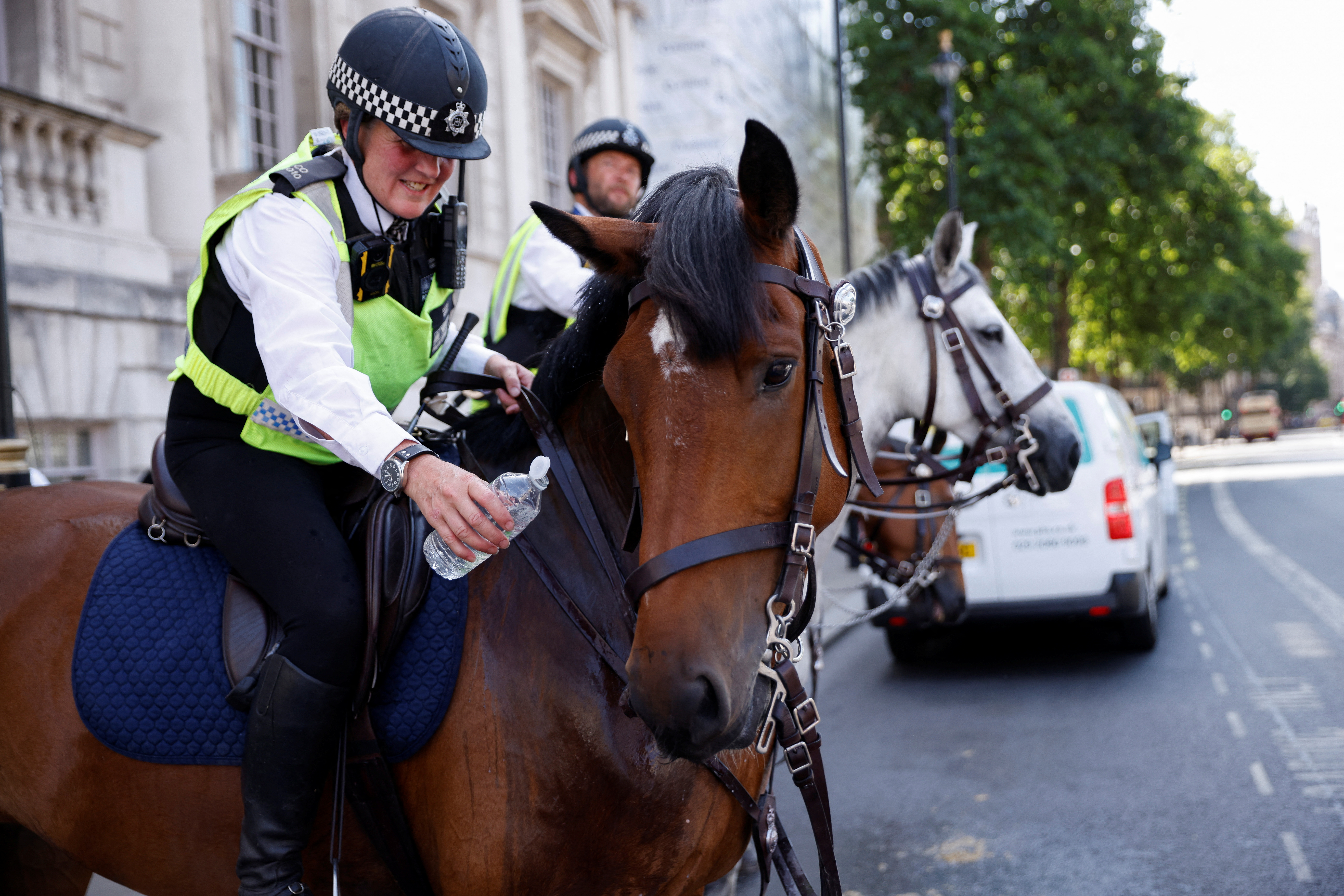 Un oficial de policía ofrece una botella de agua a un caballo de la policía llamado Zack durante el clima caluroso, en Whitehall en Londres, Gran Bretaña, el 18 de julio de 2022 (REUTERS/John Sibley)