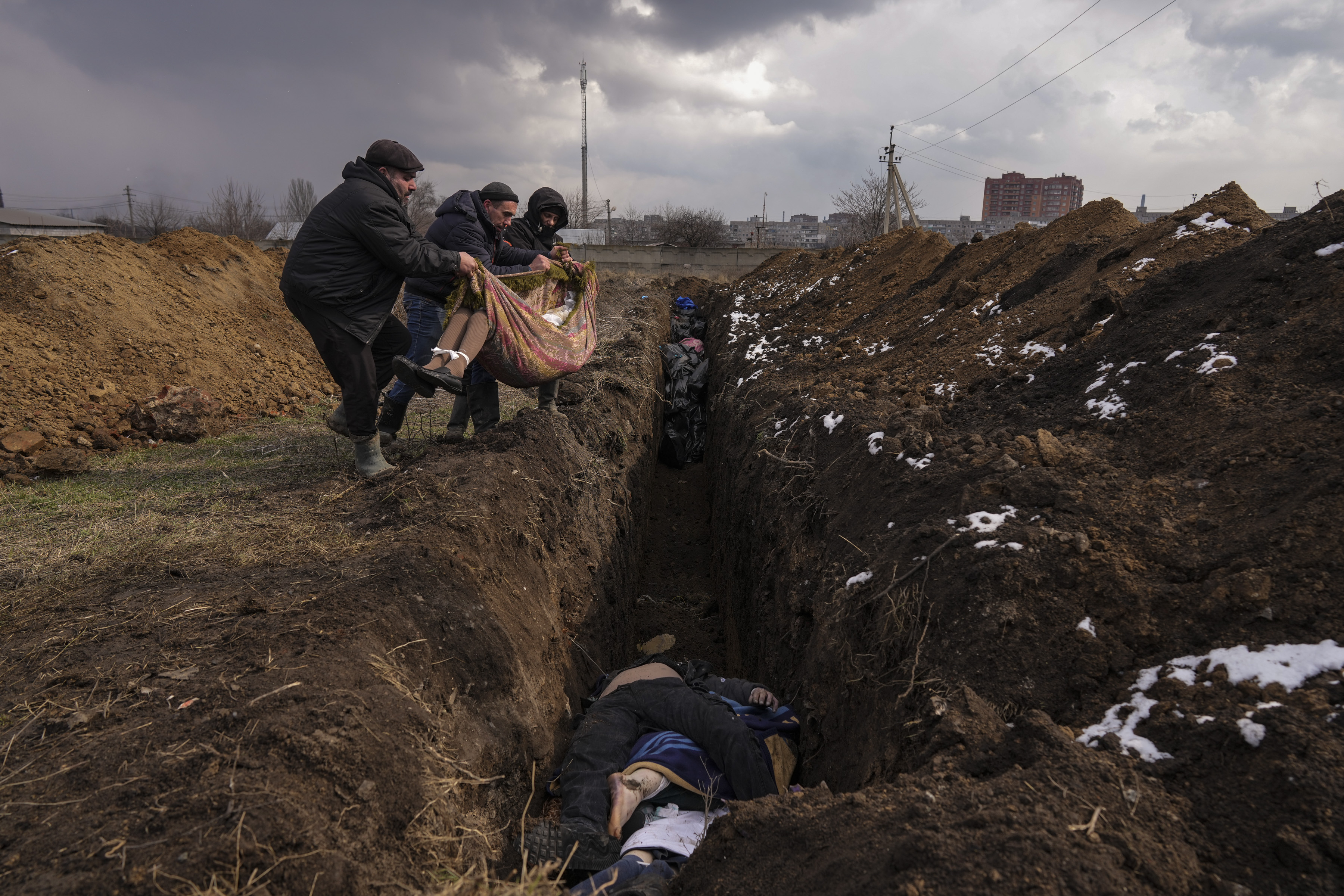 Varias personas arrojan un cadáver a una fosa común a las afueras de Mariúpol, Ucrania, el 9 de marzo de 2022. (AP Foto/Evgeniy Maloletka)