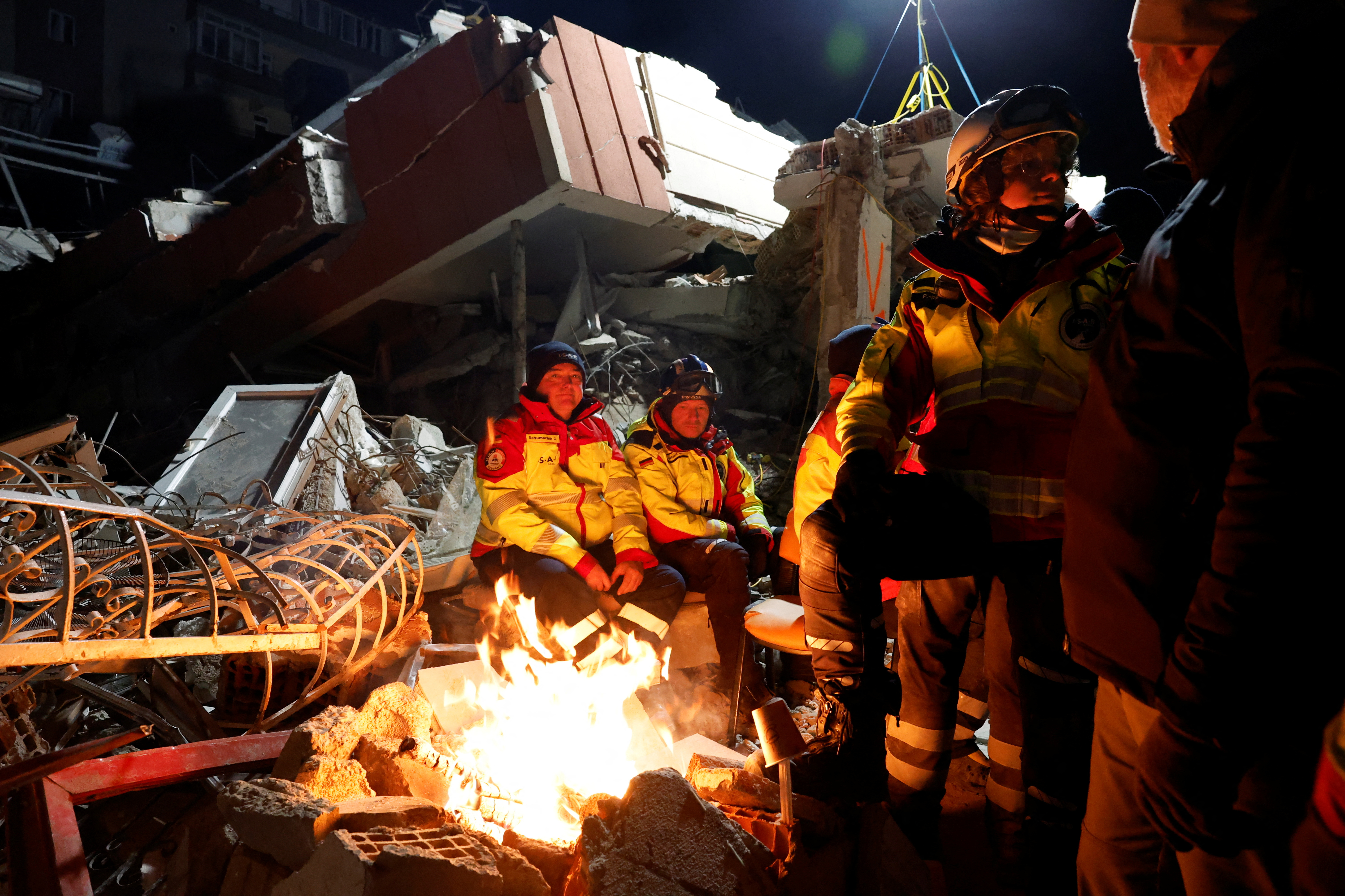 Members of Germany's ISAR rescue team warm up by a bonfire in Kirikhan, Turkey, February 10, 2023. REUTERS/Piroschka van de Wouw