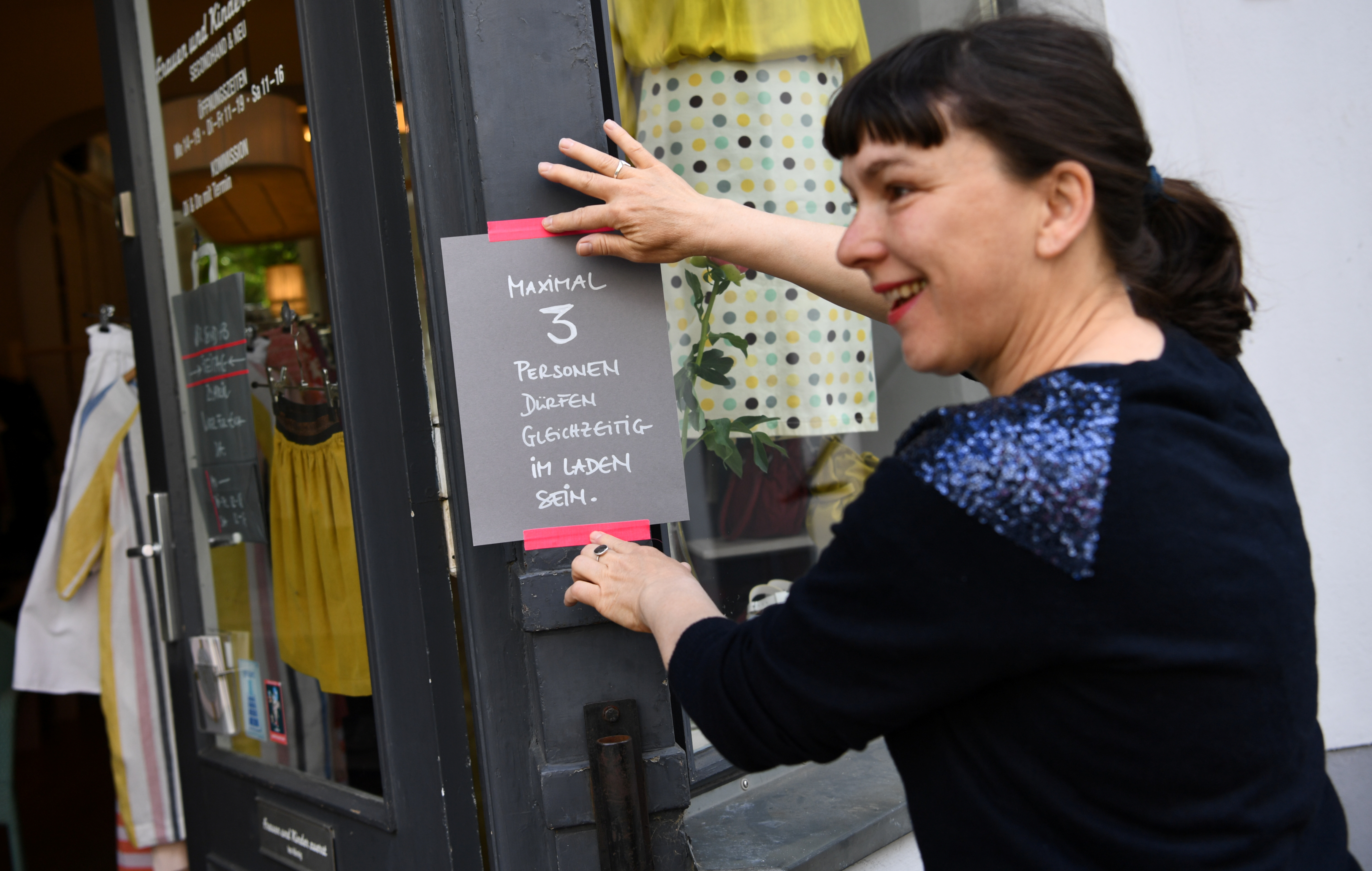 Babette Schumacher, vendedora de la tienda de ropa ''Frauen und Kinder zuerst'', cuelga un letrero que indica el distanciamiento social en Berlín, Alemania, el 25 de abril de 2020.  (REUTERS/Annegret Hilse)