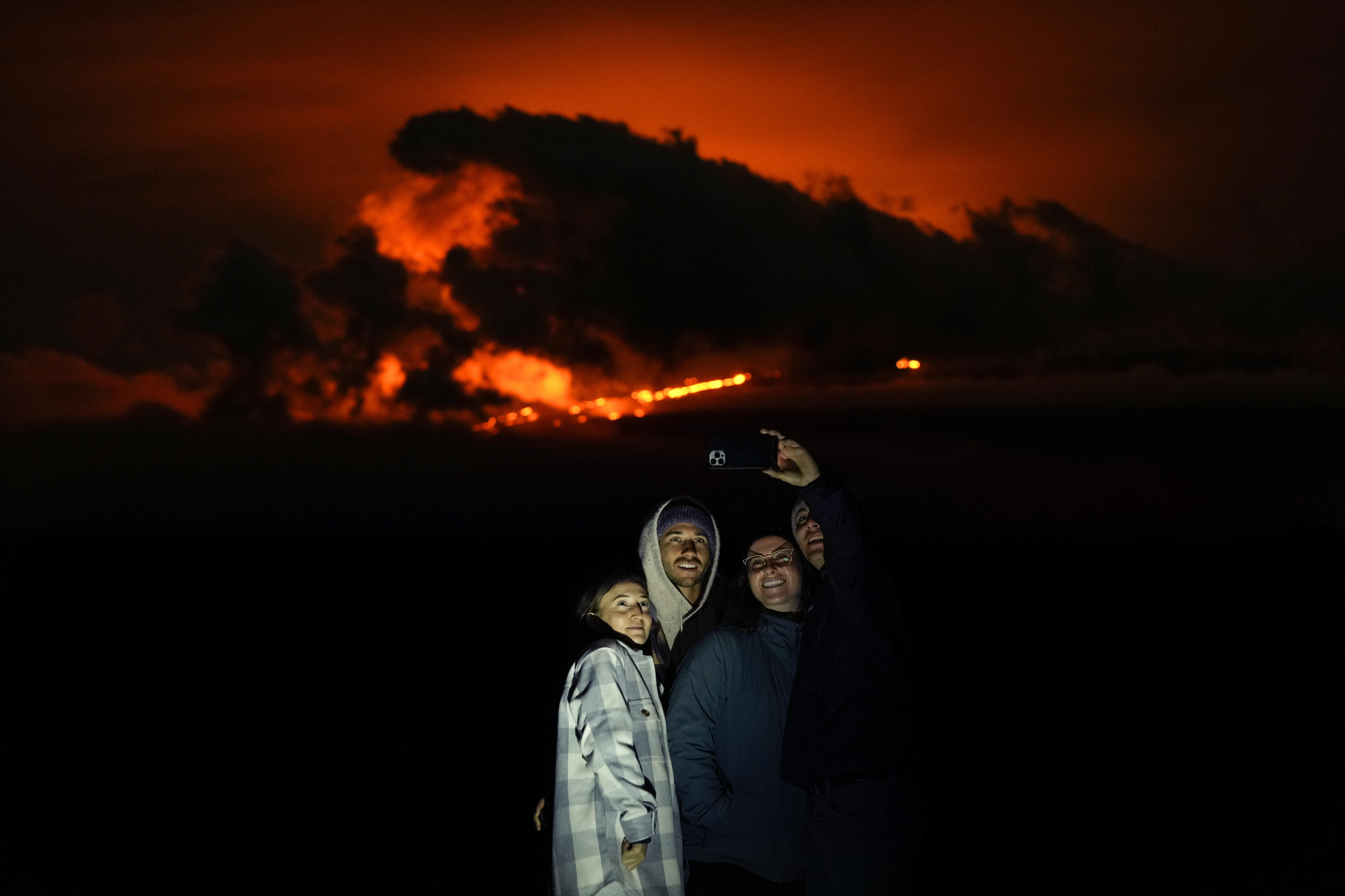 Ashlyn Nadeau, a la izquierda, junto a su esposo, Casey Nadeau, segundo desde la izquierda; Jessica Doyle, segunda desde la derecha, y Justin Potter, a la derecha, mientras toman una foto debajo del volcán Mauna Loa en erupción el viernes, cerca de Hilo, Hawái. (Foto AP/Gregory Bull)