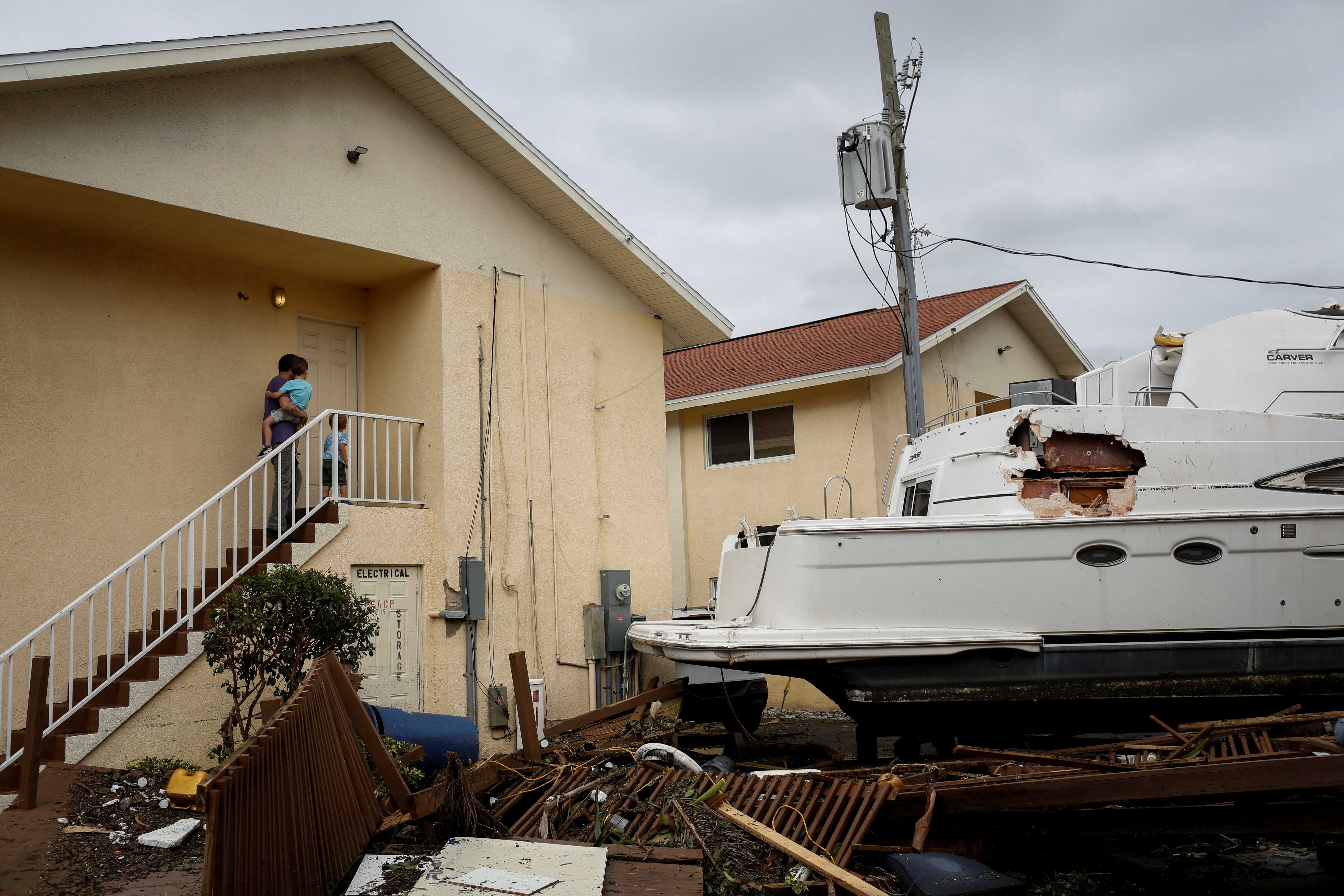 Un hombre con dos pequeños sube las escaleras, al lado un bote dañado en medio de un condominio después de que el huracán Ian causara una destrucción generalizada, en Fort Myers, Florida, el 29 de septiembre de 2022. (REUTERS/Marco Bello)