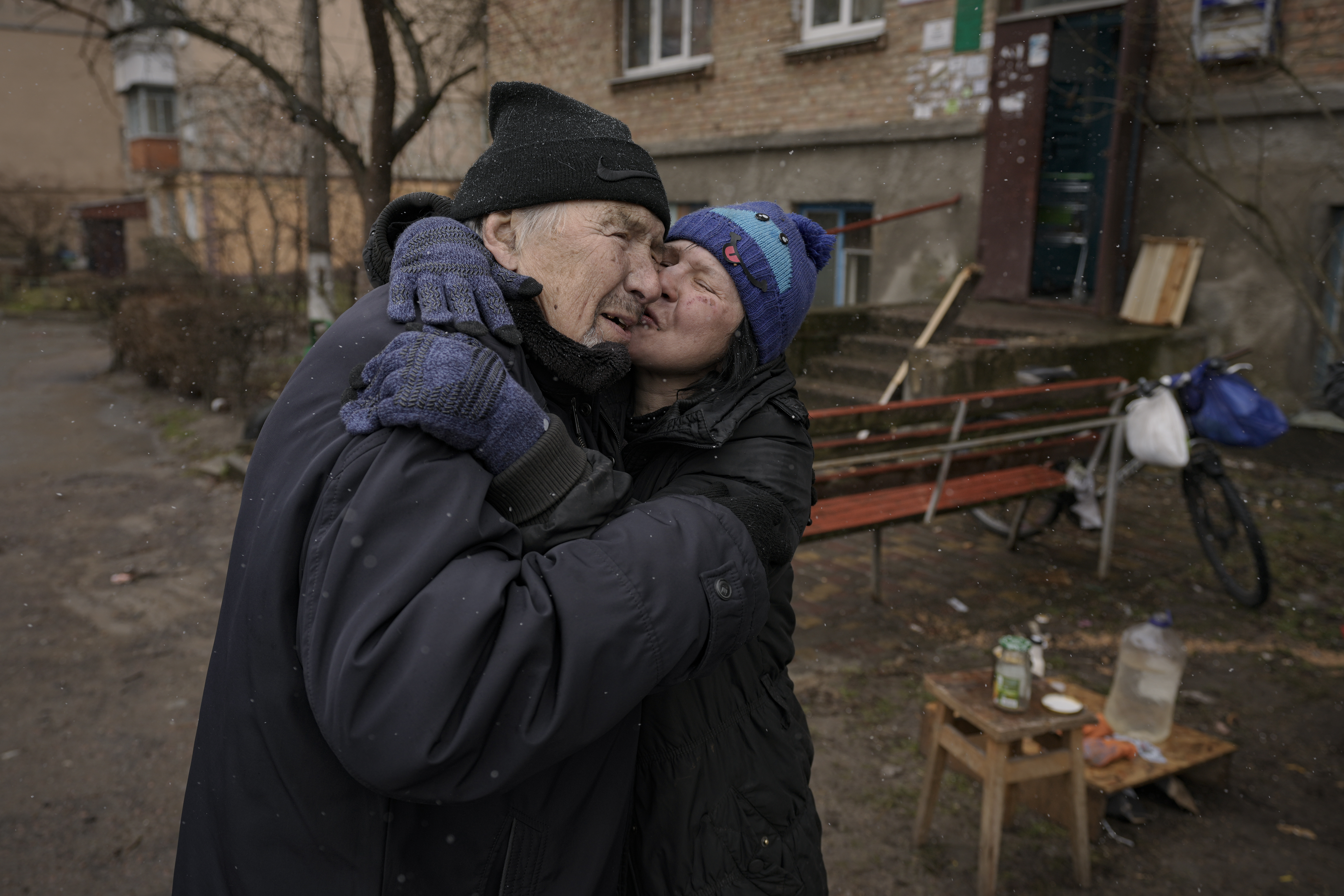 Una mujer besa a un hombre mientras cocina en una hoguera en el exterior de un edificio de apartamentos que no tenía electricidad, agua ni gas desde el comienzo de la invasión rusa en Bucha, Ucrania, el domingo 3 de abril de 2022. (AP Foto/Vadim Ghirda)