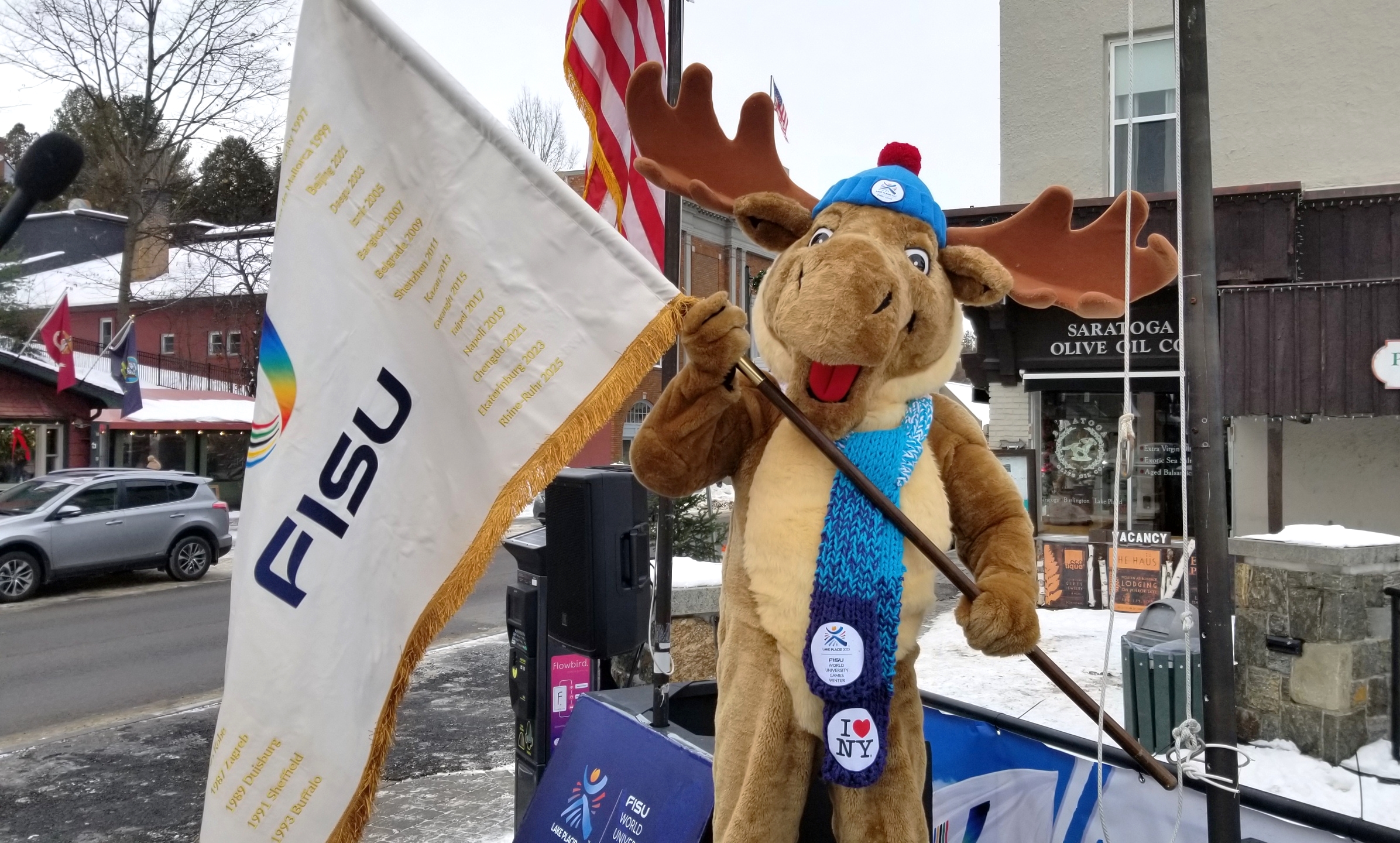 The Lake Placid 2023 FISU World University Games’ official mascot Adirondack Mac proudly waves the FISU Flag. Photo courtesy of Lake Placid 2023 FISU World University Games.