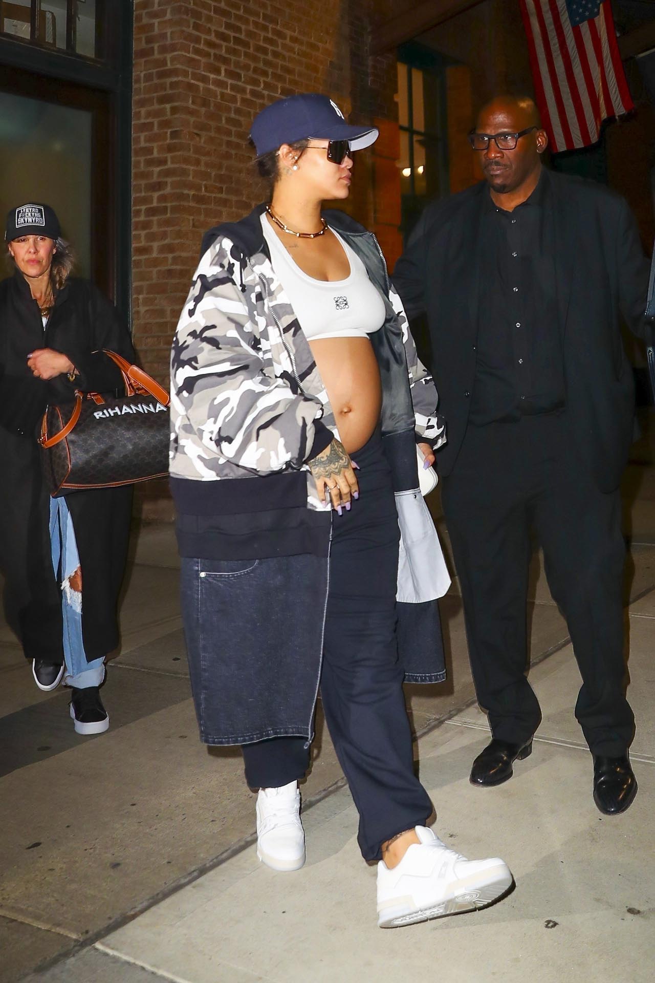 Rihanna fue fotografiada antes de tomar un avión privado en Nueva York. La artista, que está embarazada esperando su segundo hijo con el rapero A$AP Rocky, lució un top blanco, pantalón de algodón con un detalle sobresalido de tela de jean, y una campera camuflada en la gama del gris y negro. Además, llevó una gorra azul. Una de sus colaboradoras, por su parte, llevó un bolso customizado con su nombre