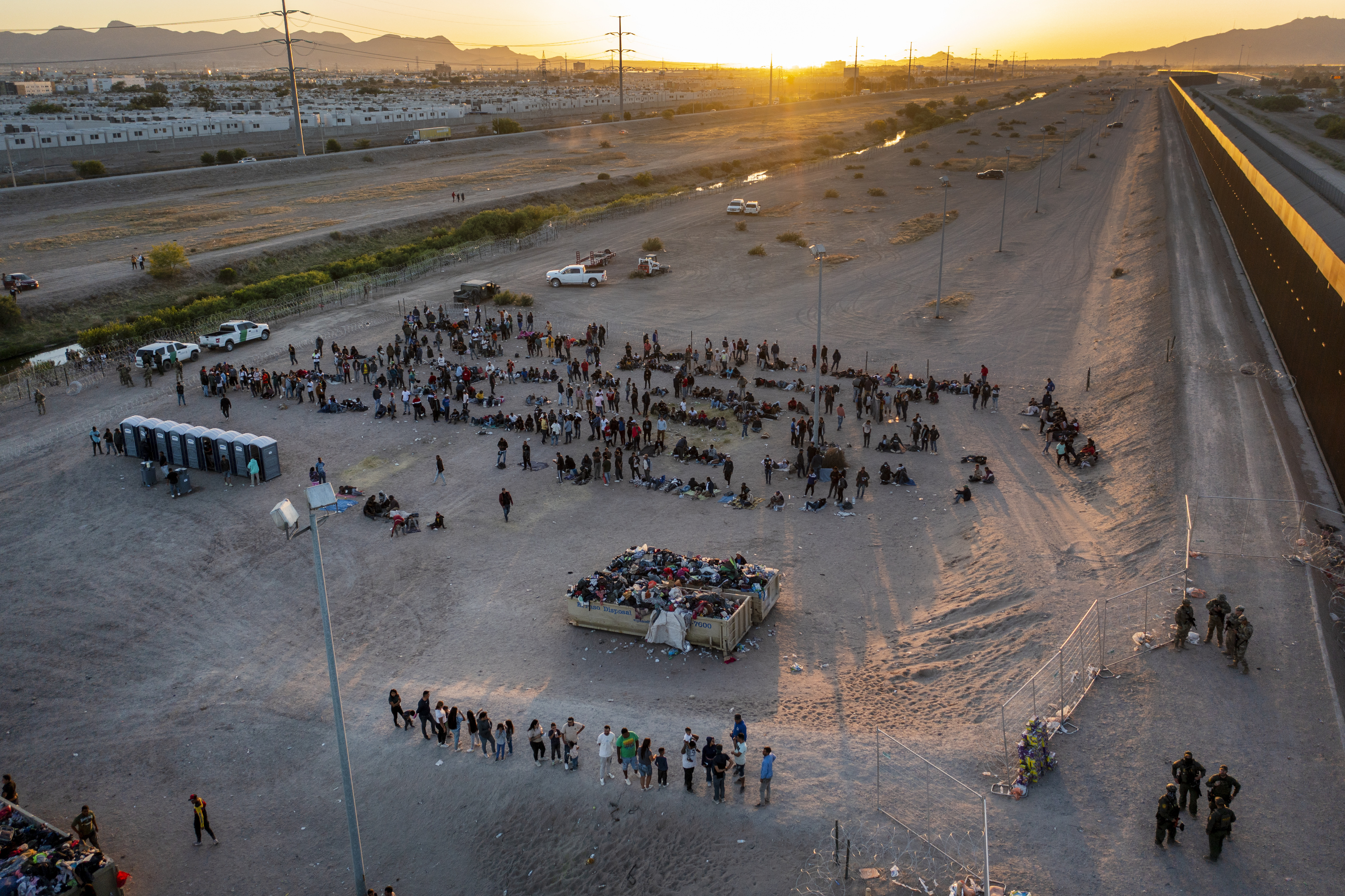 A medida que el sol se pone, migrantes aguardan afuera de una puerta en la cerca fronteriza el jueves 11 de mayo de 2023 para ingresar a El Paso, Texas, con el fin de que la Patrulla Fronteriza procese sus casos. Gran cantidad de migrantes se apresuraron a cruzar la frontera con México, en un intento apresurado por ingresar a Estados Unidos antes de que llegara a su fin una norma que restringía el asilo, en un cambio de política que amenaza con agobiar aún más el sistema migratorio de Estados Unidos. (AP Foto/Andrés Leighton)