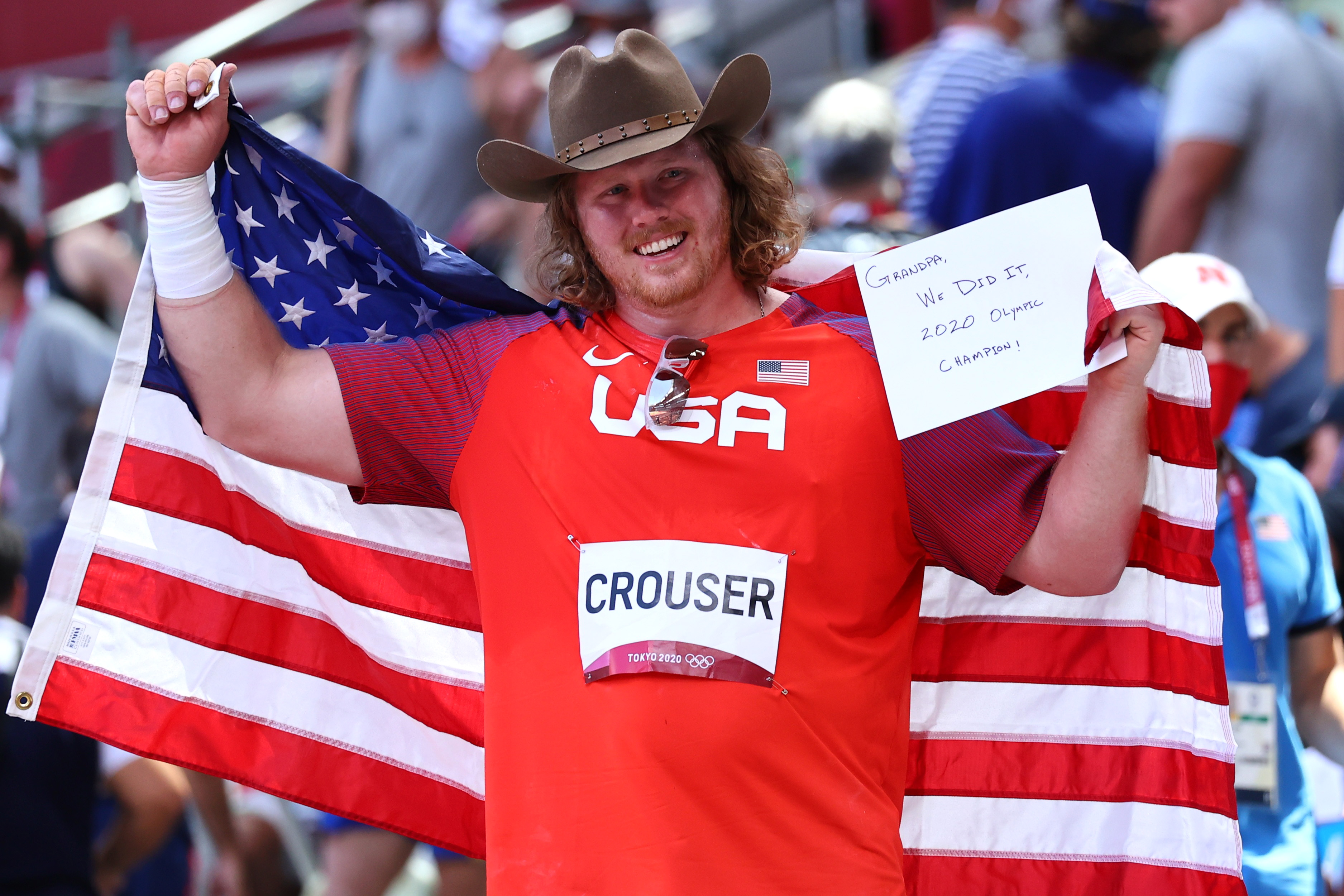 Tokyo 2020 Olympics - Athletics - Men's Shot Put - Final - Olympic Stadium, Tokyo, Japan - August 5, 2021. Ryan Crouser of the United States holds a note in reference to his grandfather as he celebrates with his national flag after winning gold REUTERS/Lucy Nicholson