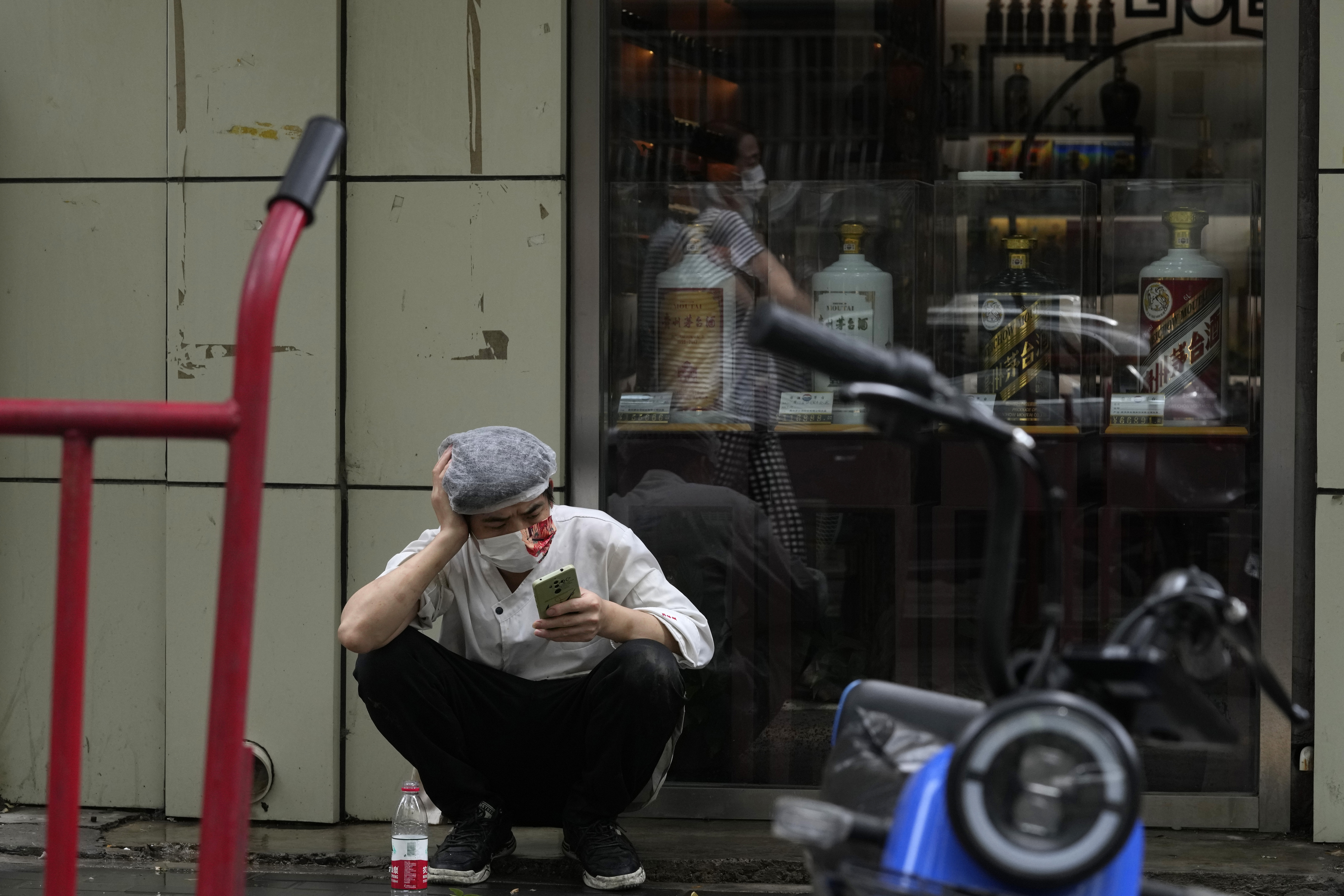 Un cocinero de restaurante con mascarilla se toma un descanso en una vereda, el lunes 27 de junio de 2022 en Beijing, China. (AP Foto/Ng Han Guan)