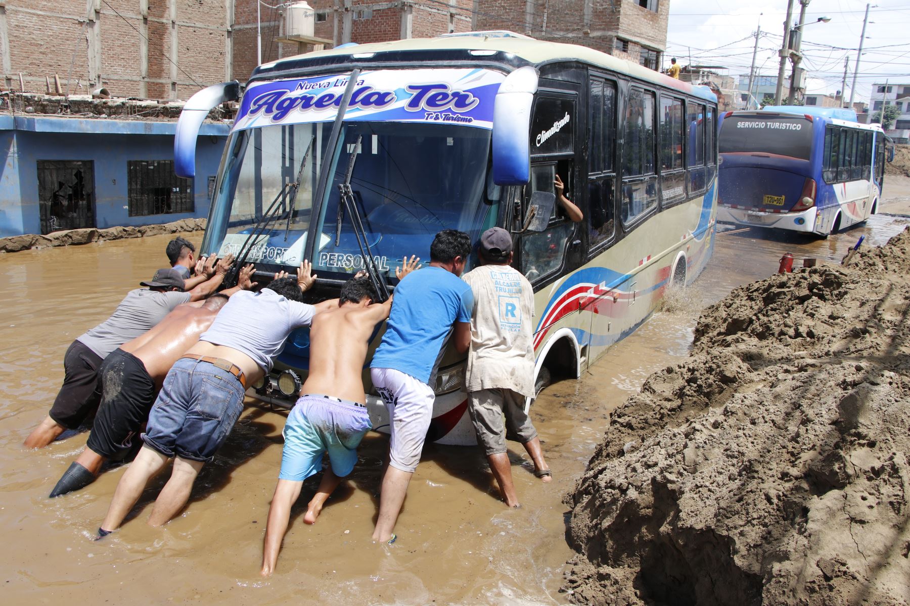 Un grupo de personas intenta sacar un bus interprovincial del lodo. 