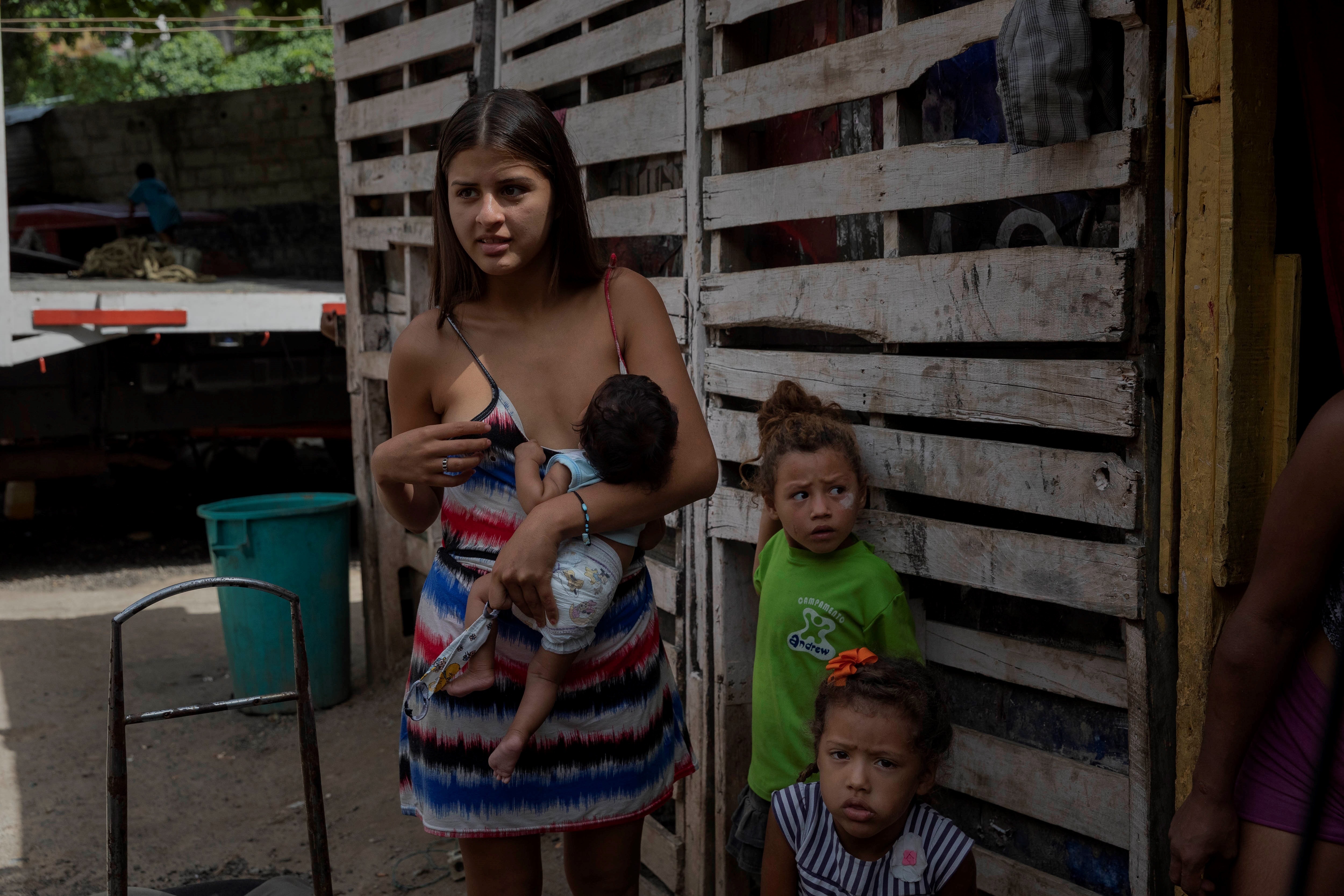 Una mujer amamanta a su hijo de tres meses frente a su vivienda improvisada en un terreno ocupado en Caracas (EFE/Archivo)
