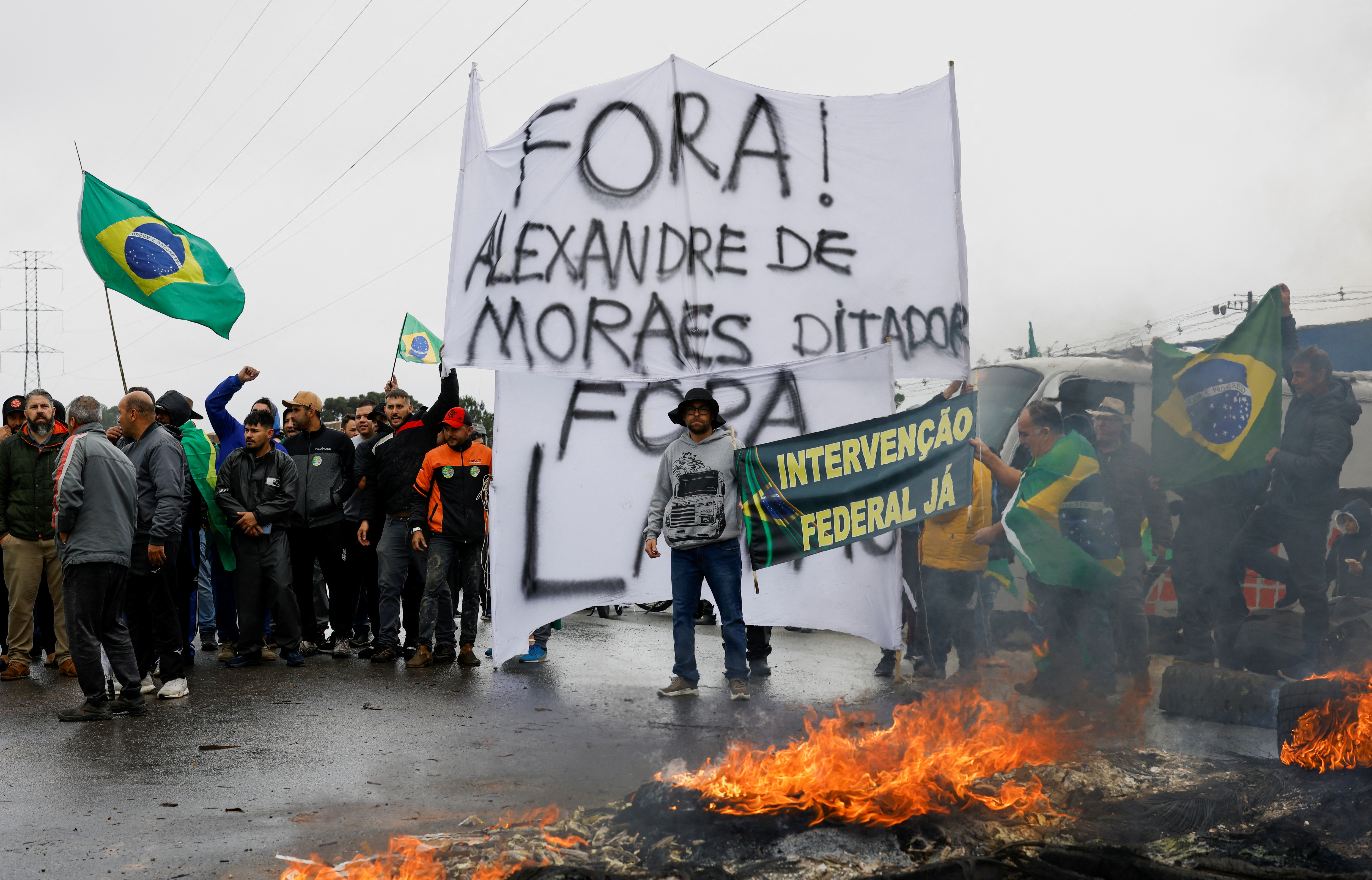 Los partidarios del presidente de Brasil, Jair Bolsonaro, en su mayoría camioneros, sostienen carteles y banderas mientras bloquean una carretera (REUTERS/Rodolfo Buhrer)