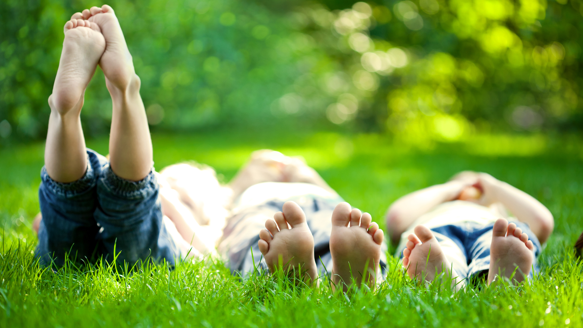 Group of happy children lying on green grass outdoors in spring park.